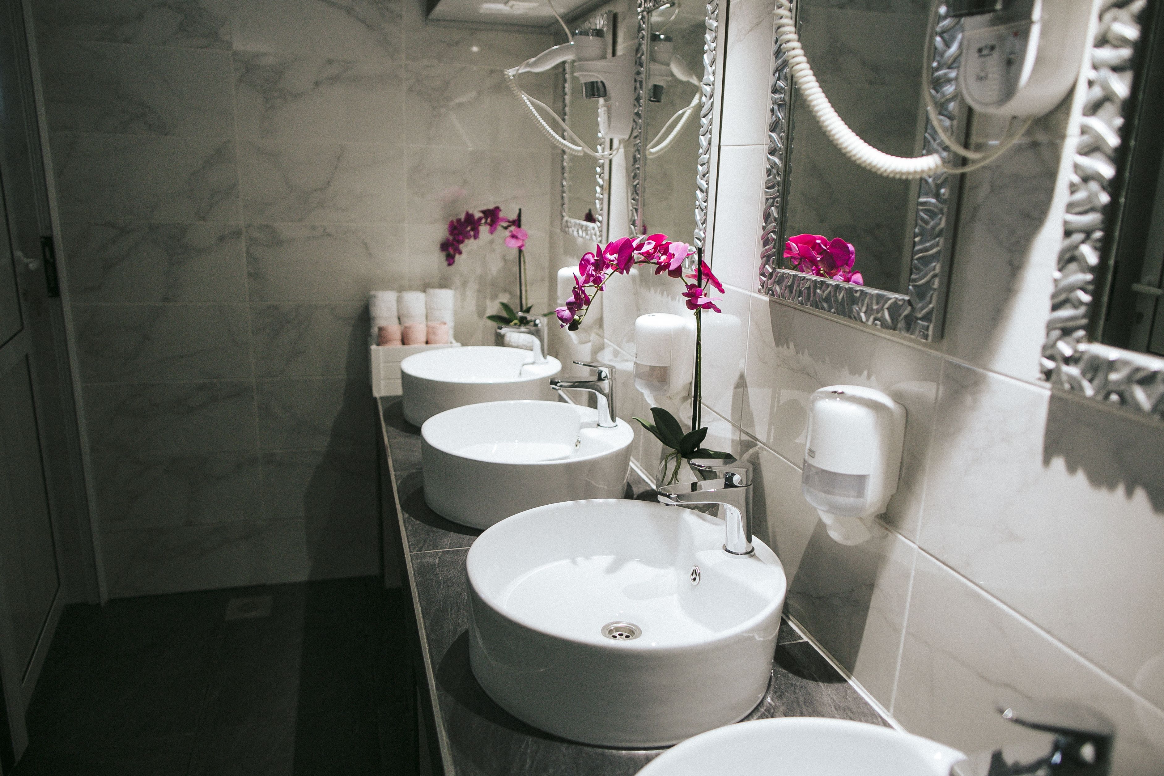 Une salle de bain moderne avec trois vasques rondes, un sèche-cheveux et un miroir doté d’un cadre décoratif.