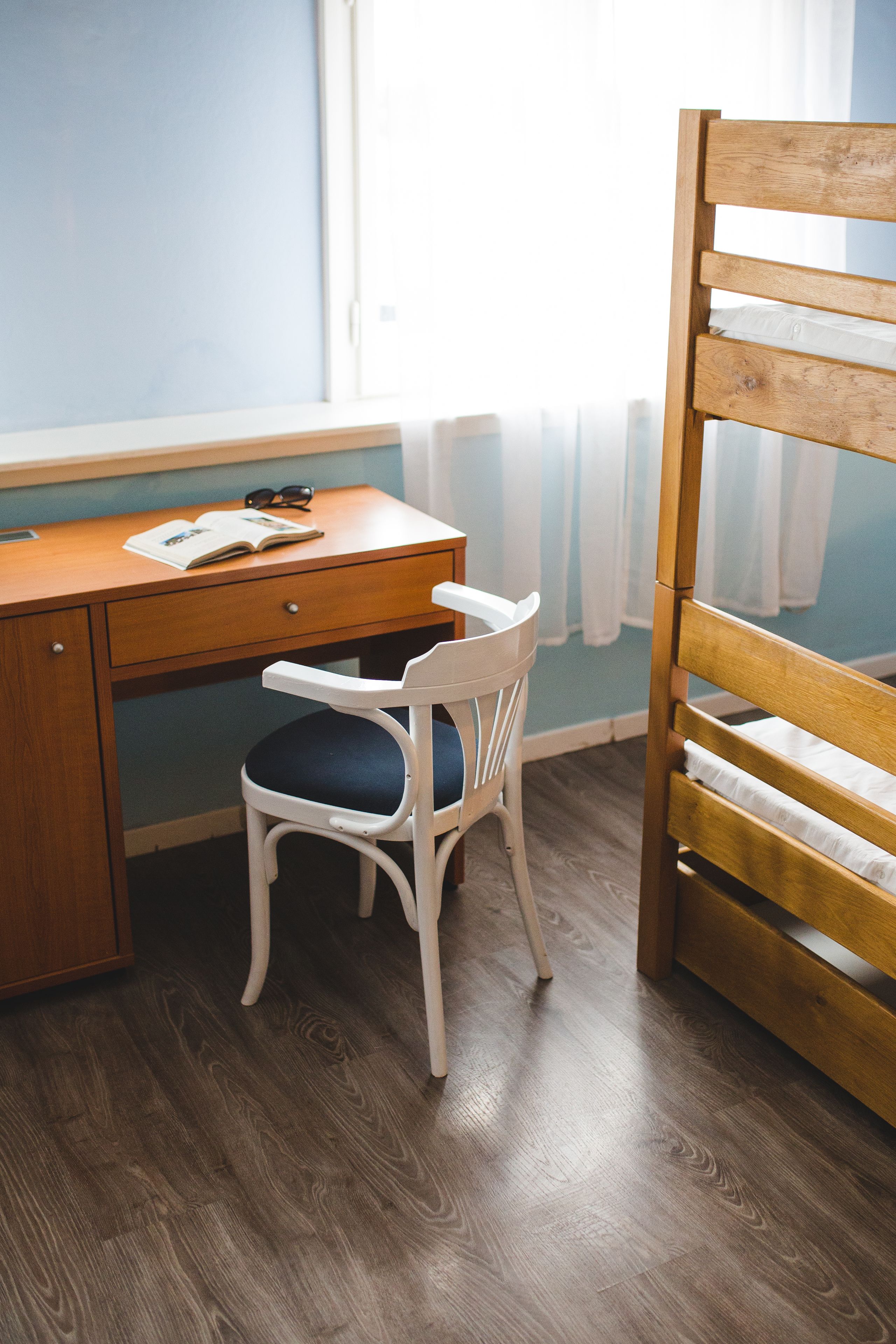 Una habitación con un escritorio de madera, una silla blanca con cojín azul y una cama nido de madera.