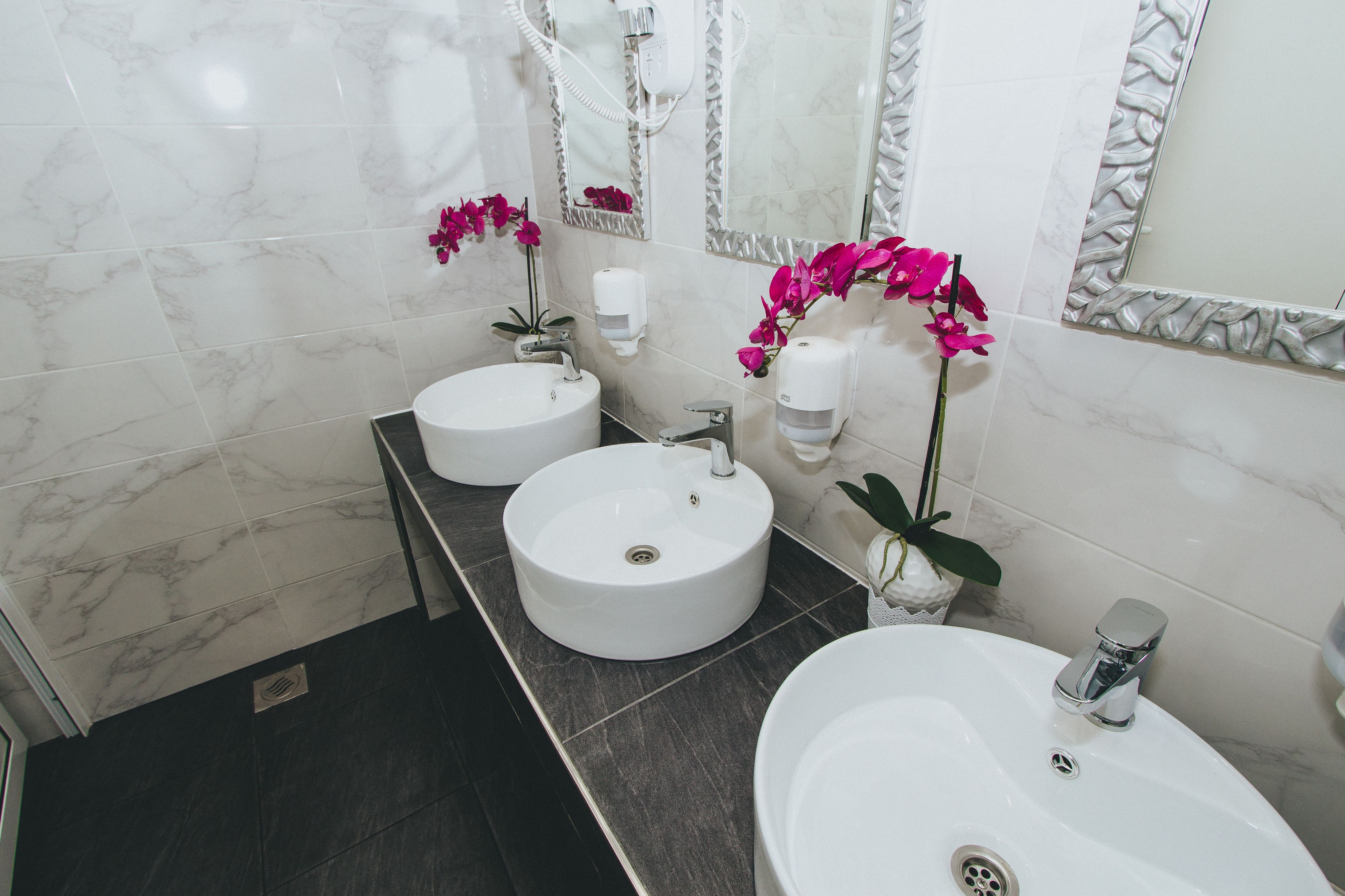 A bathroom with two sinks, marble tiles, and pink orchids.