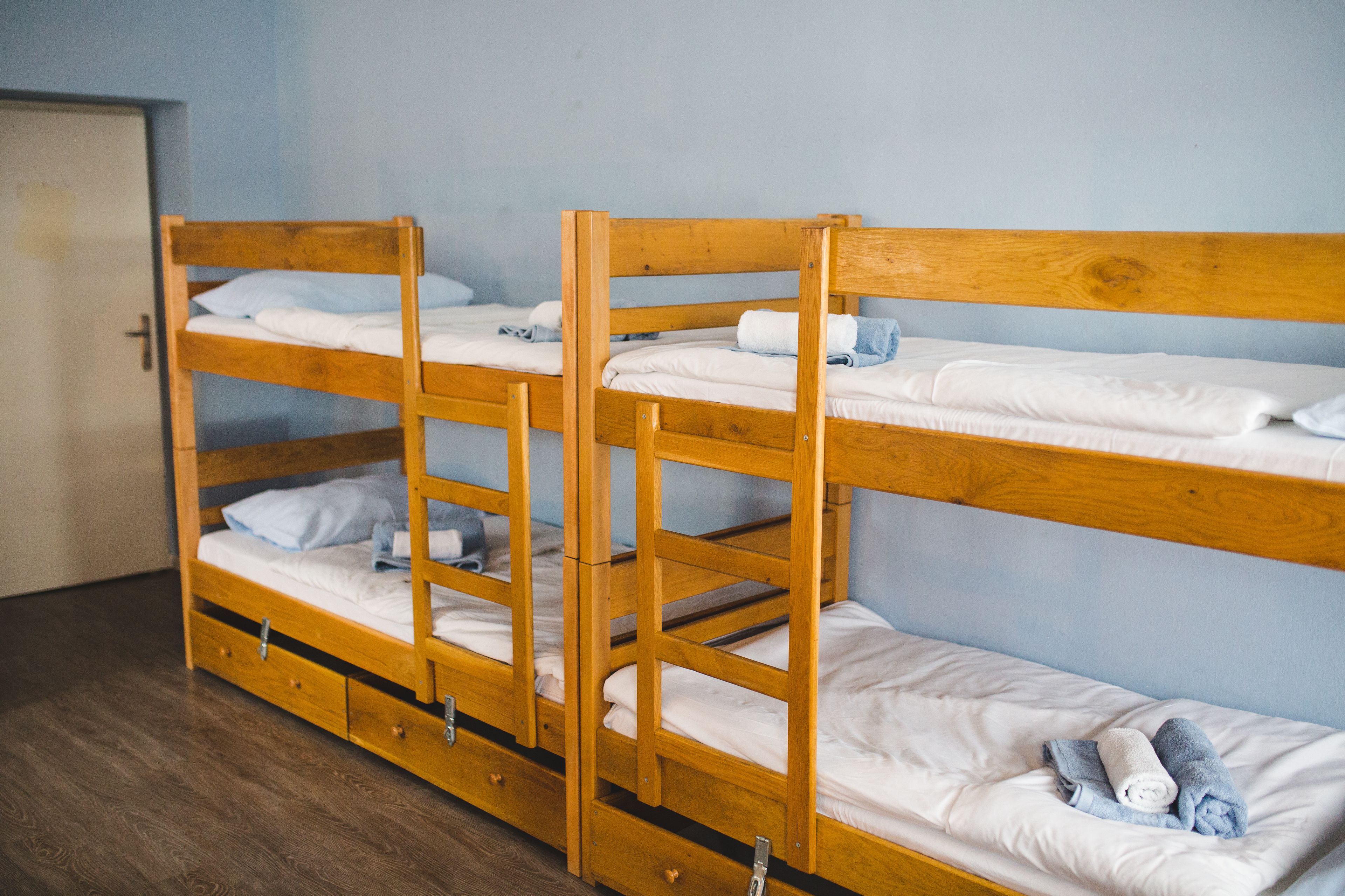 A bunk bed room with wooden frames, white bedding, and a door.