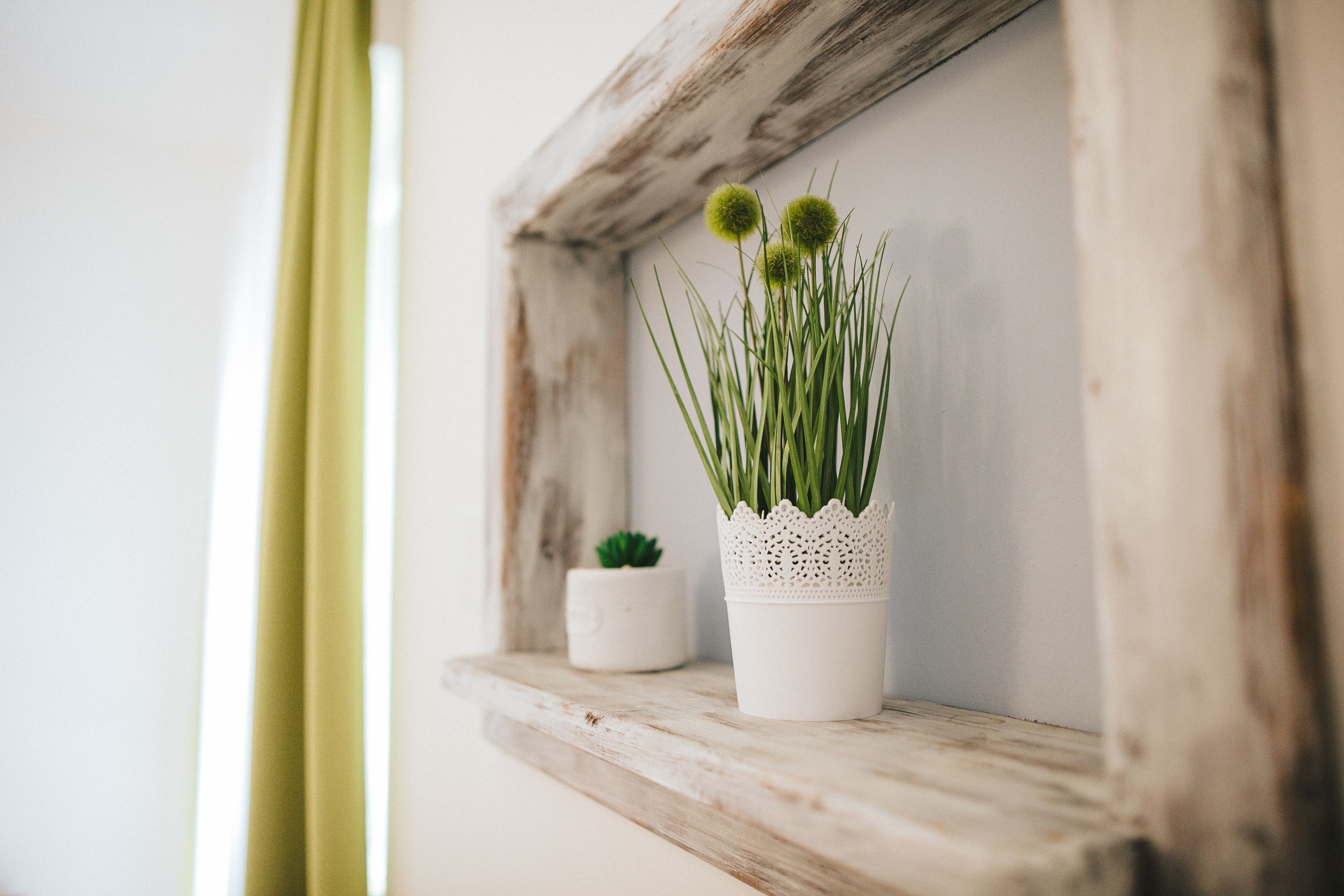 A rustic wooden shelf with a white pot containing green plants and a small potted plant.
