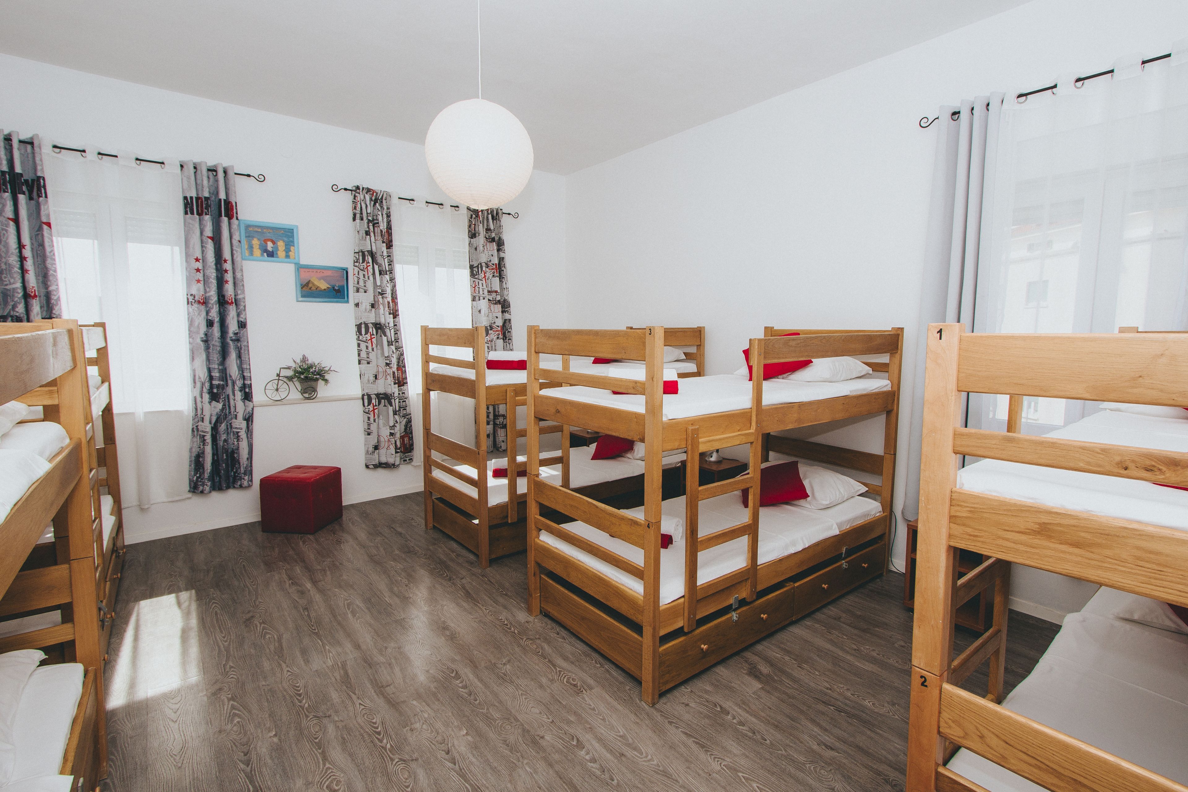 Quarto com beliches, um banquinho vermelho e luminária pendente.