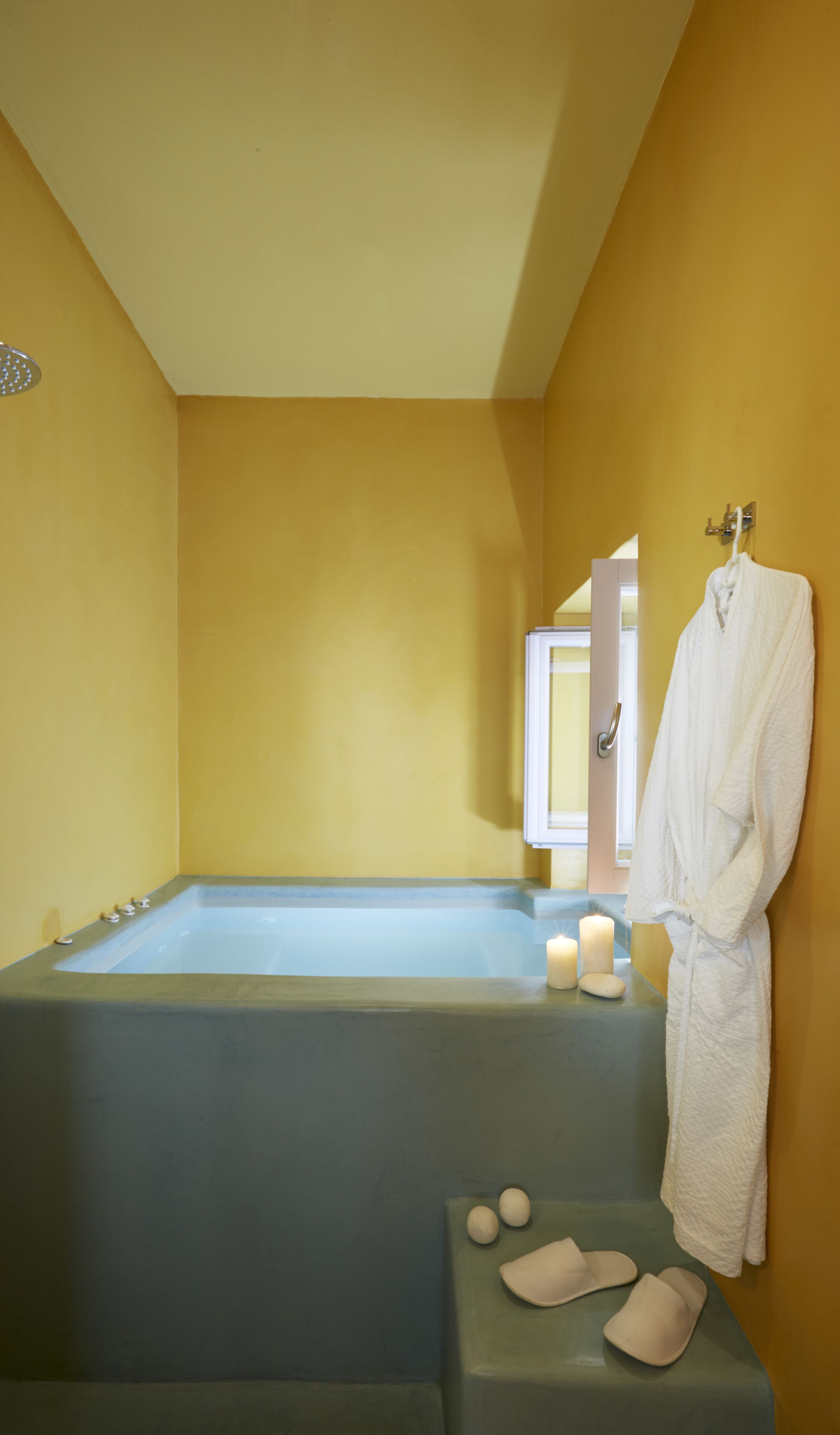 A bathroom with a bathtub, a towel rack with a robe, and two candles on the edge of the tub.