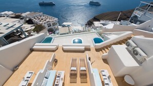 A sun deck with lounge chairs and a pool, overlooking a body of water with boats. - On the Cliff (Santorini)