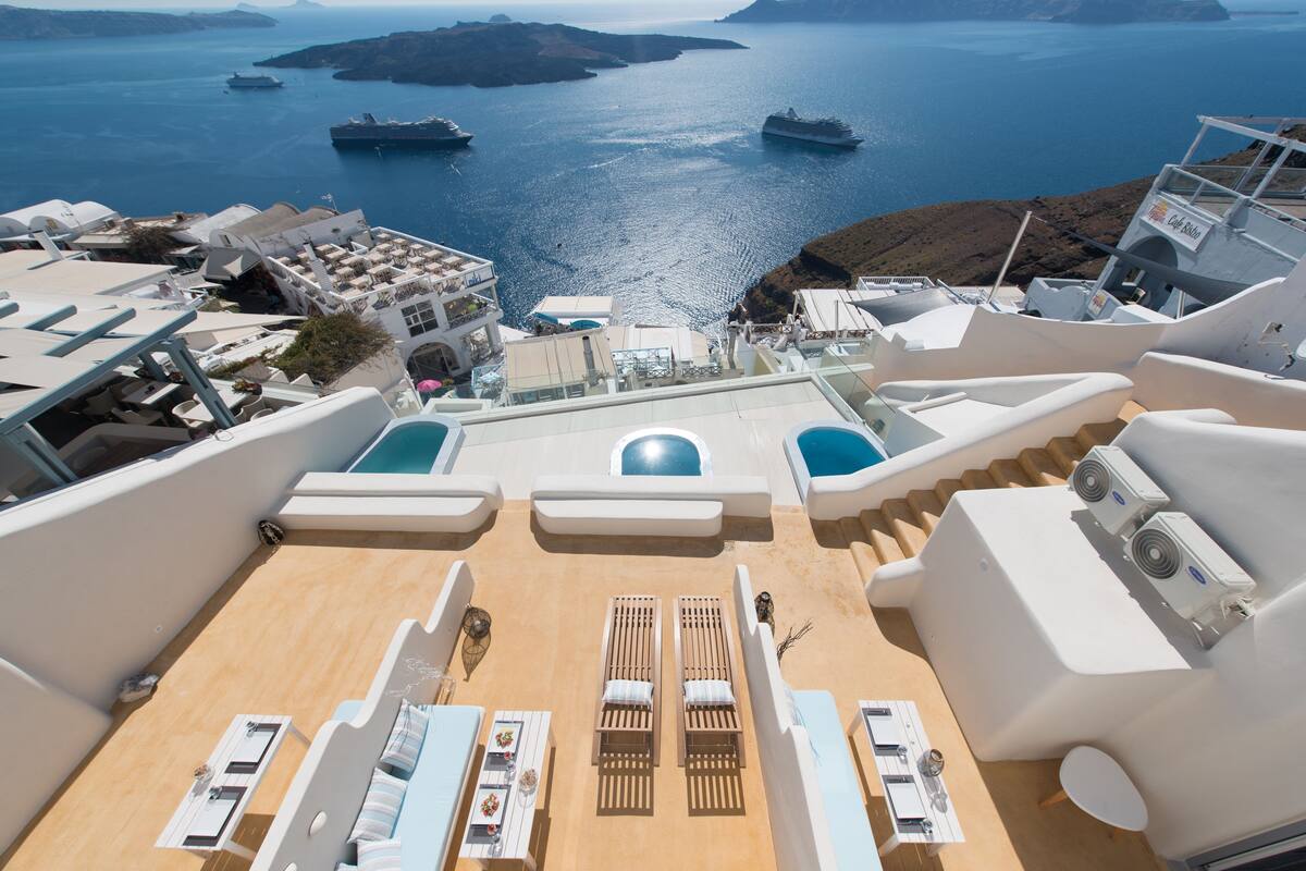 Une terrasse ensoleillée avec des chaises longues et une piscine, offrant une vue sur une étendue d’eau où naviguent des bateaux.
