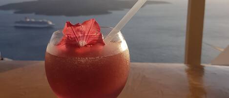 A cocktail with a straw and a decorative leaf on a table with a view of the sea and a ship in the distance.
