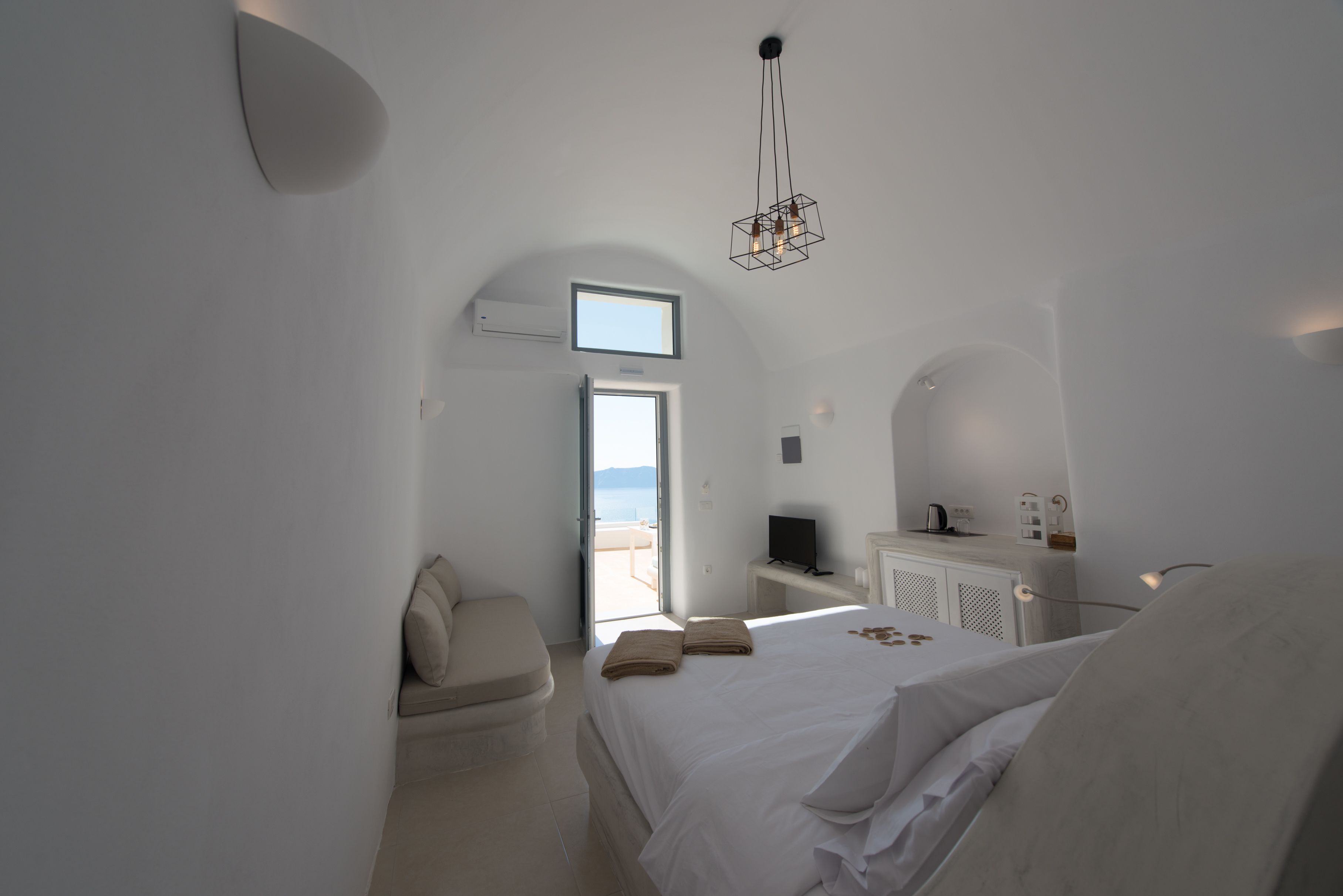 A modern bedroom with a bed, a seating area, a TV, and a view of the outdoors.