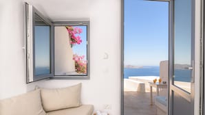 A room with a sofa, a bedside table with a phone, and a window with a view of the sea. - On the Cliff (Santorini)