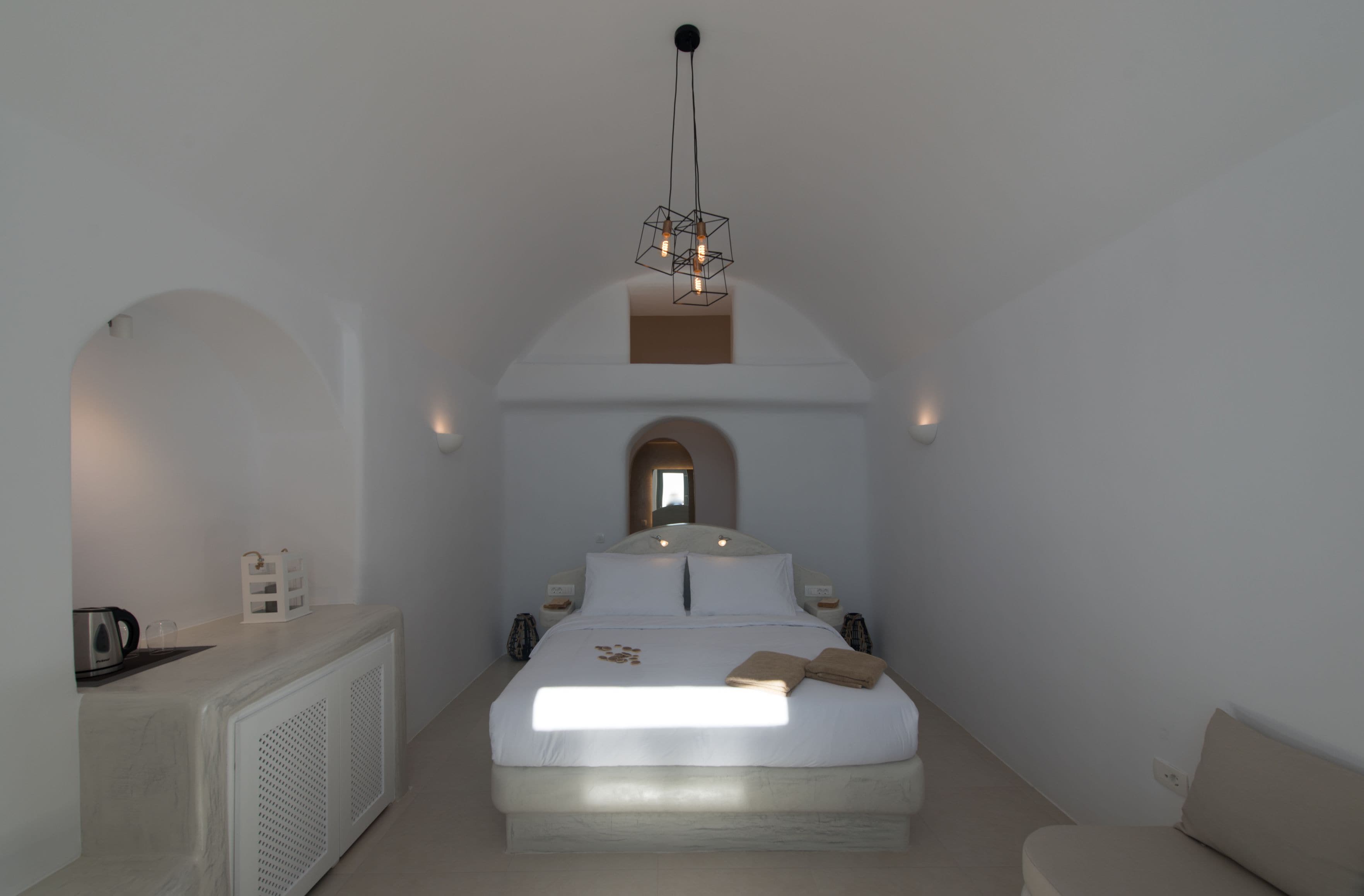 A bedroom with a large bed, a small table with a kettle, and a unique ceiling light fixture.