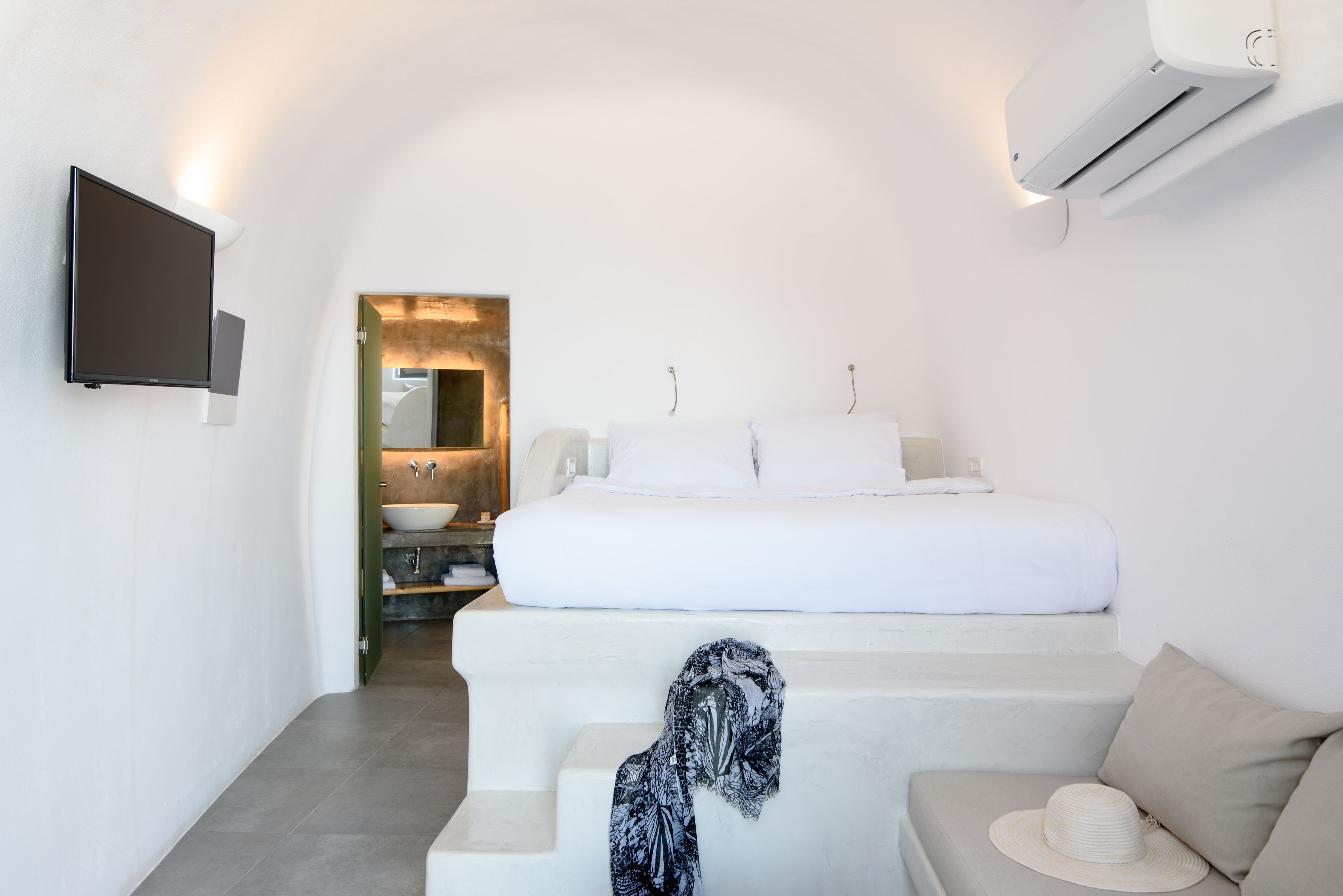 A modern bedroom with a bed, a sofa, a TV, and an air conditioning unit.