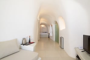A hotel corridor with a sofa, a coffee machine, a TV, and a phone on a desk. - On the Cliff (Santorini)