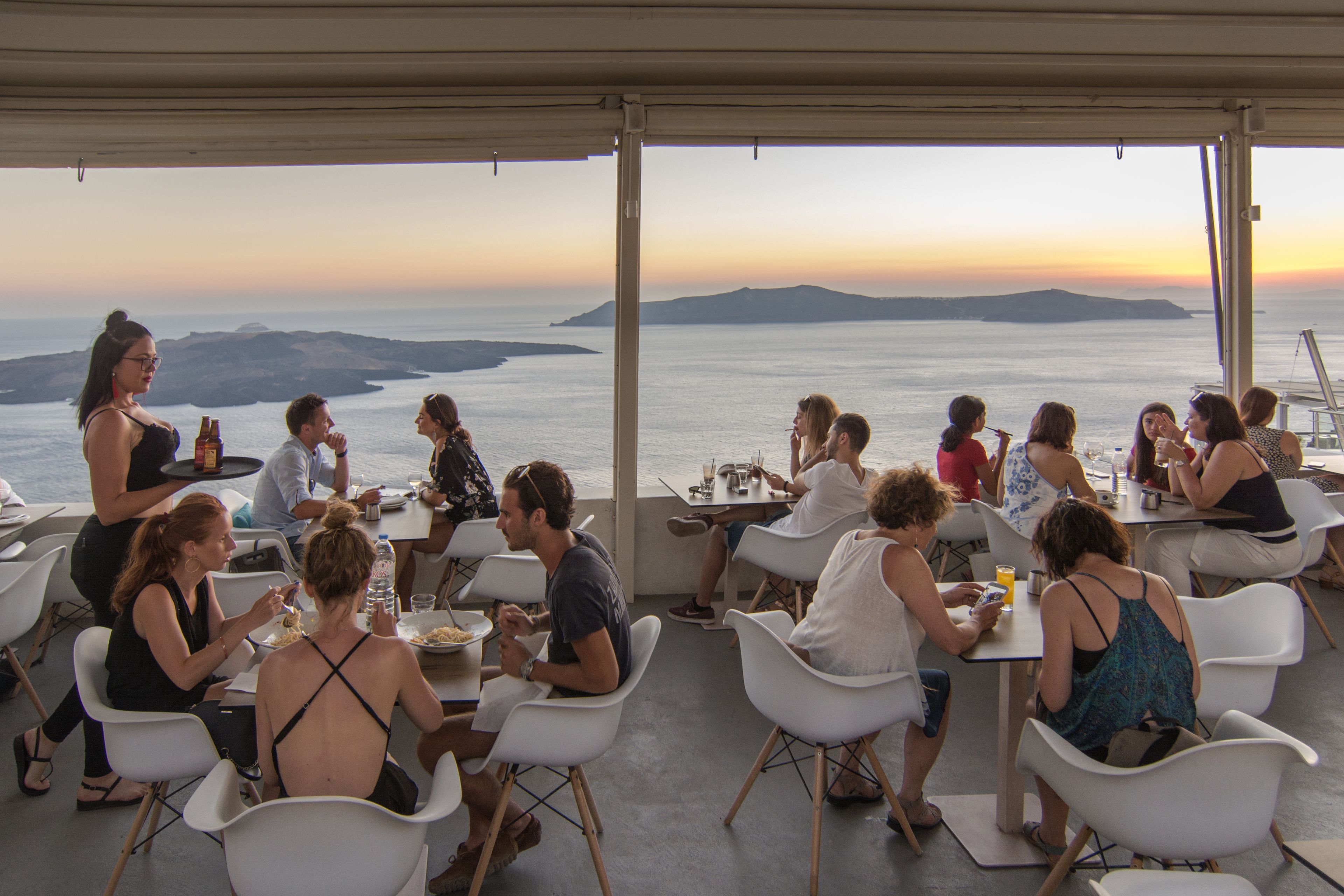 A restaurant with outdoor seating overlooking a scenic view of the ocean and hills.