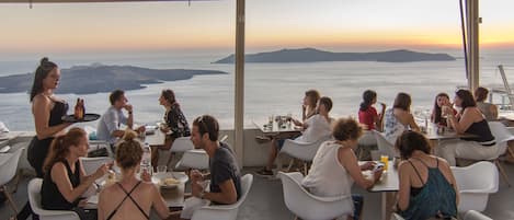 A restaurant with outdoor seating overlooking a scenic view of the ocean and hills.