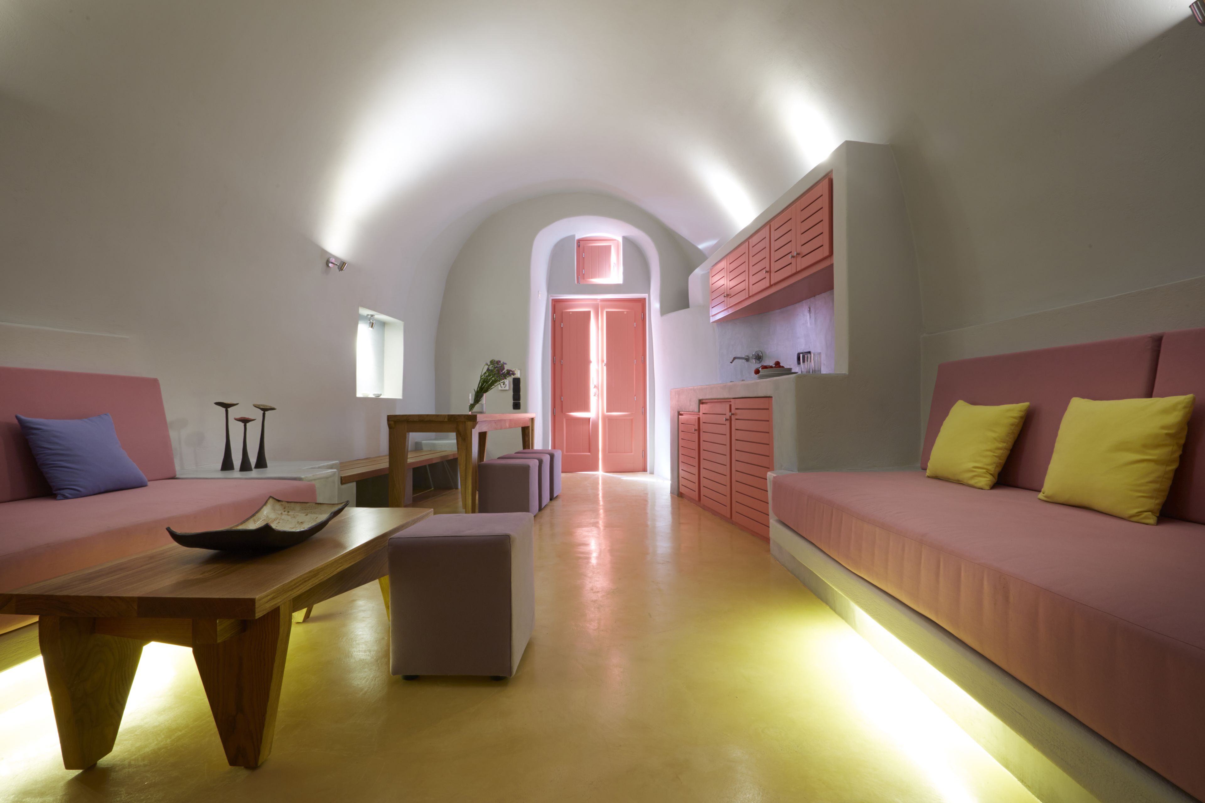 A modern interior with a wooden table, pink sofas, and a kitchen area.