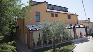 Una casa a due piani con tetto in tegole, un camino in mattoni e un portico coperto con tende bianche.