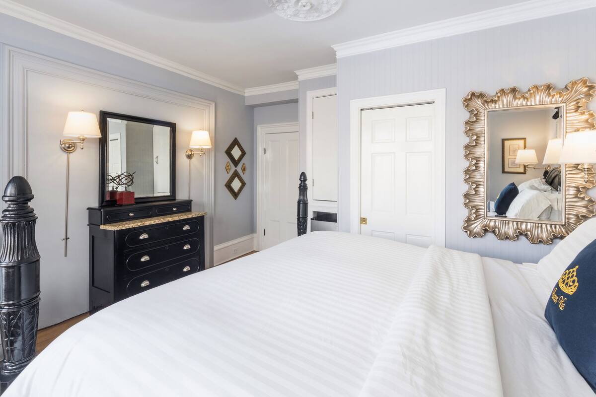 A hotel room with a large bed, a dresser, a mirror, and a door.