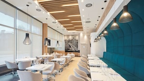 Een modern restaurant met lange tafels, stoelen en hanglampen.