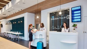 Zona de recepción de hotel con diseño moderno, que incluye un mostrador de recepción, un directorio digital y un área de estar con mesas y sillas.