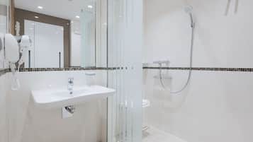 A modern bathroom with a glass shower enclosure, a white sink, and a hairdryer on the counter.