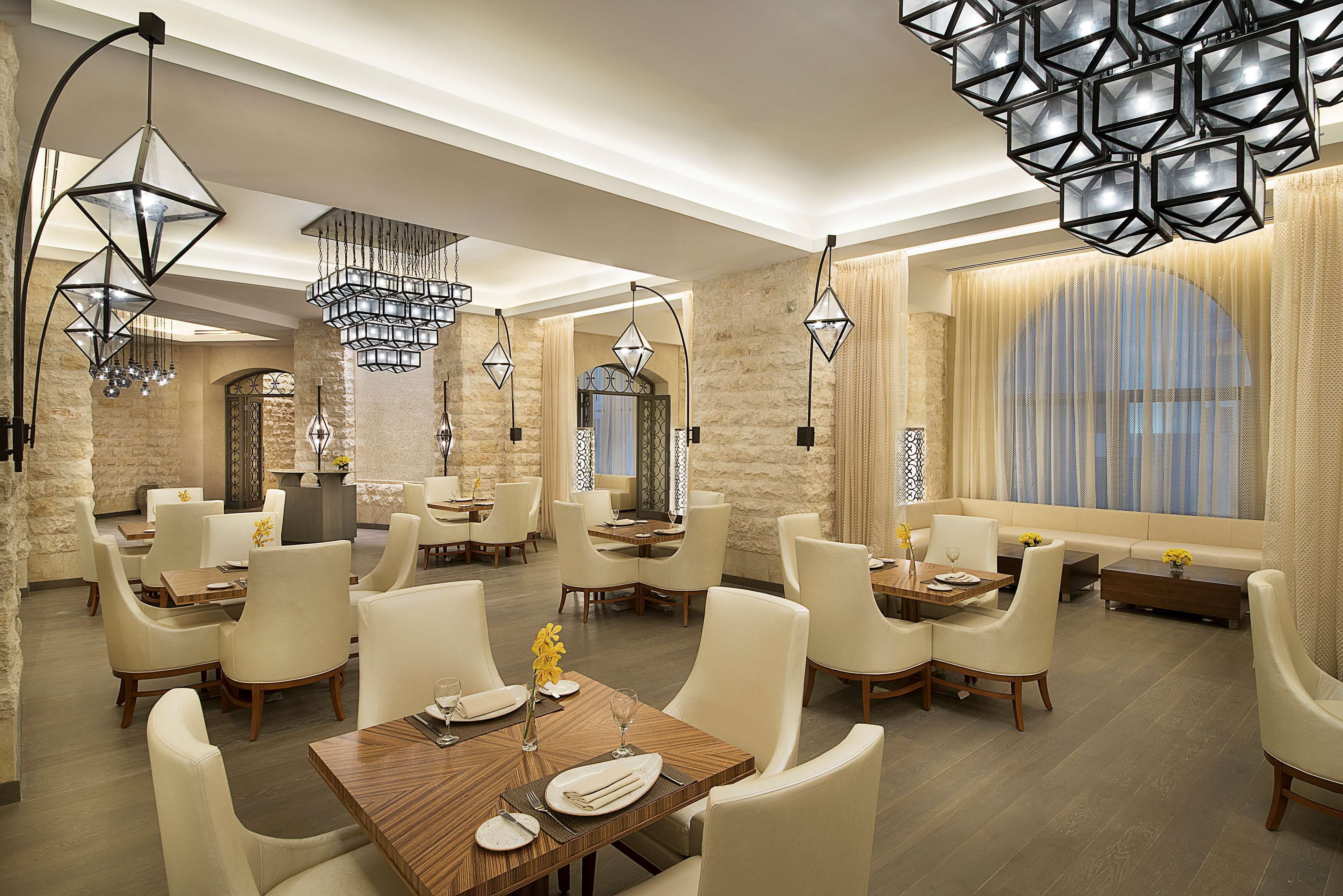 A modern dining area with multiple tables and chairs, elegant lighting fixtures, and a stone wall backdrop.