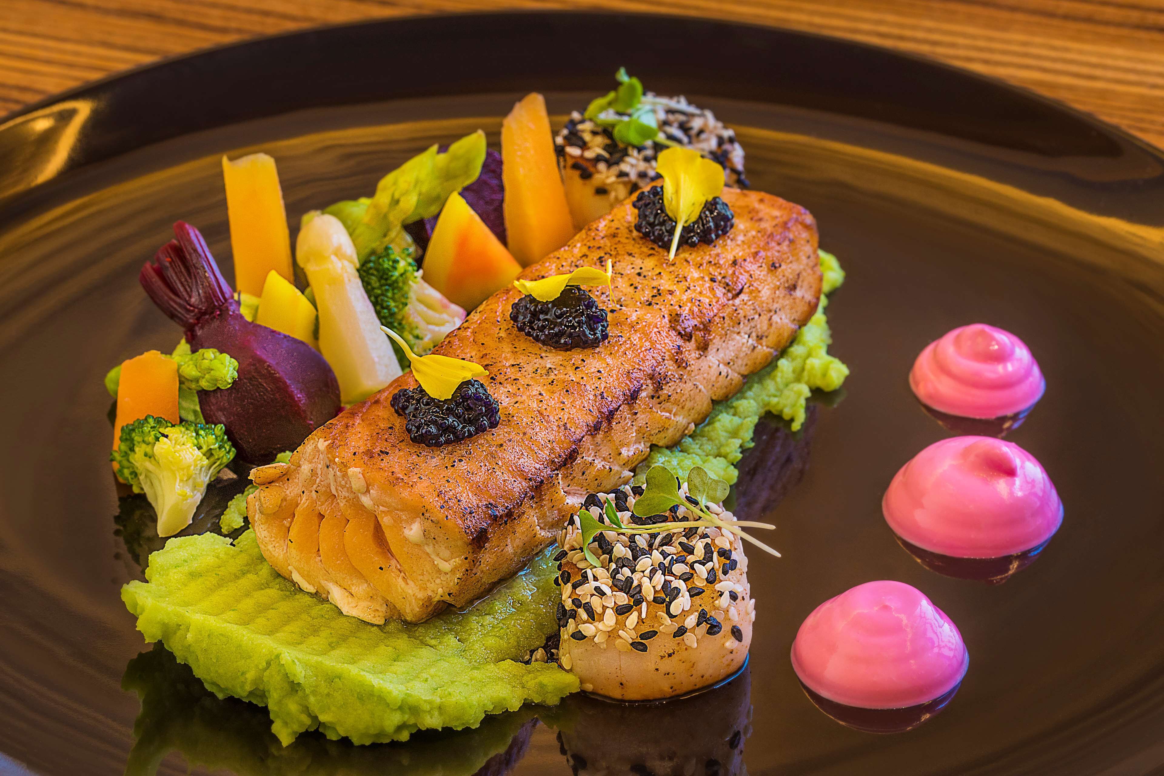 A salmon dish with various vegetables and garnishes on a plate.