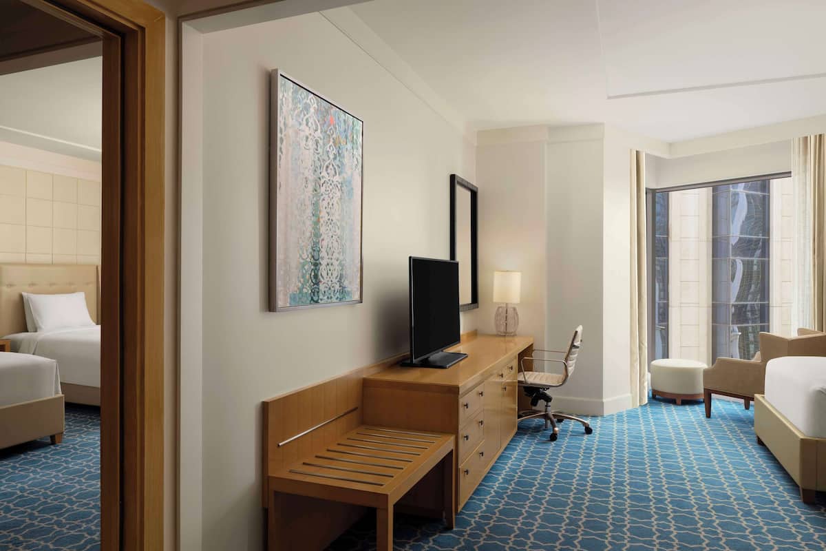 A hotel room with a bed, a desk with a chair, a television, and a large window.