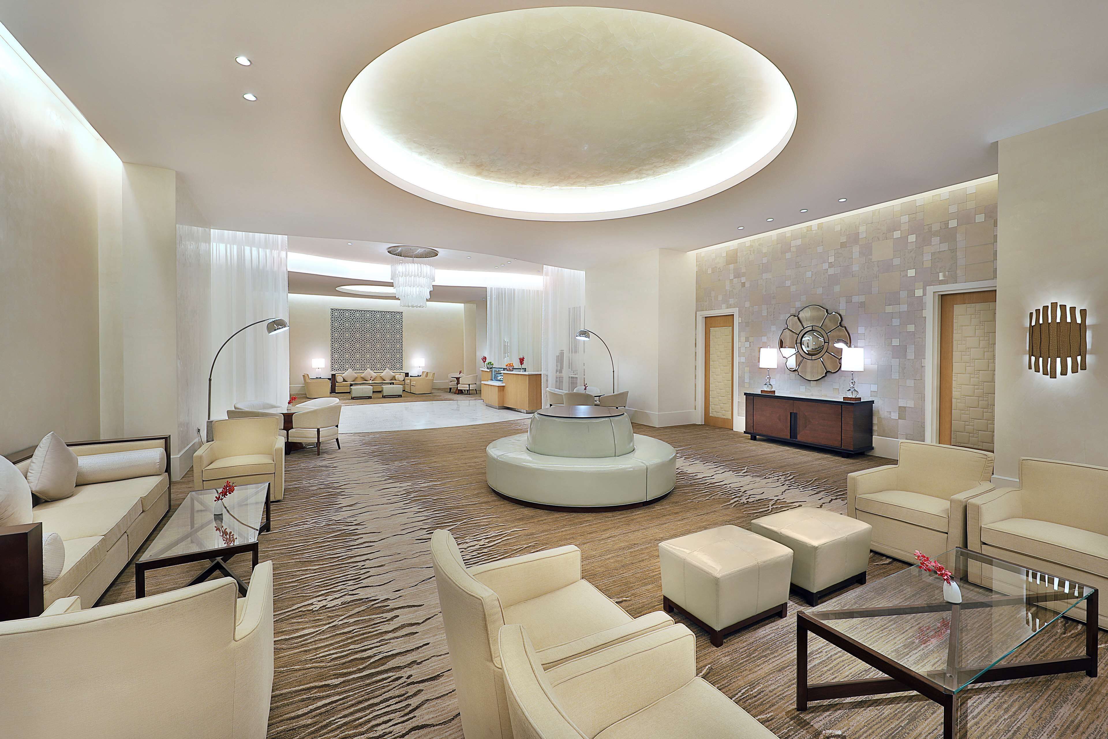 A spacious lobby with a central round table, multiple seating areas, and a modern ceiling design.