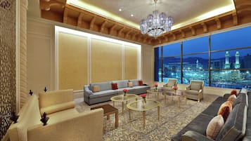 A spacious lounge with a large sofa, armchairs, and a coffee table, featuring a city view through large windows.