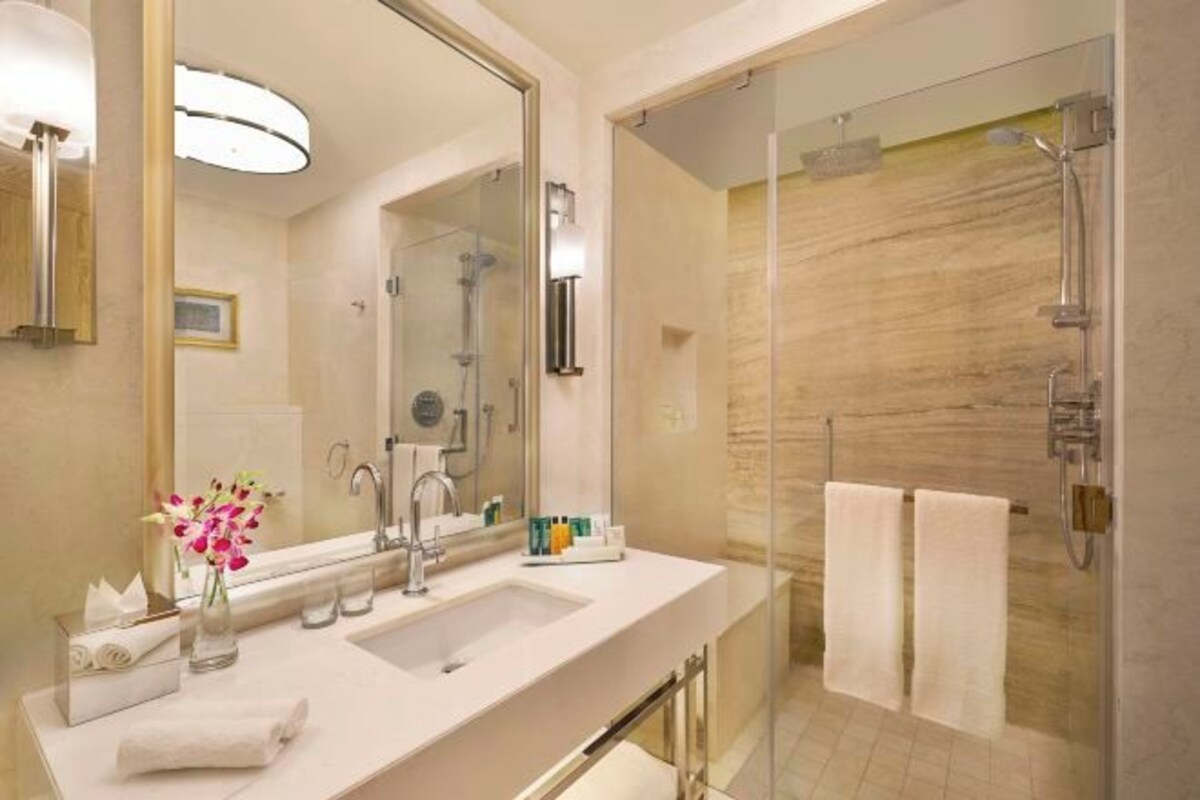 A modern bathroom with a glass-enclosed shower, a large mirror, and a vanity with a sink and towel rack.