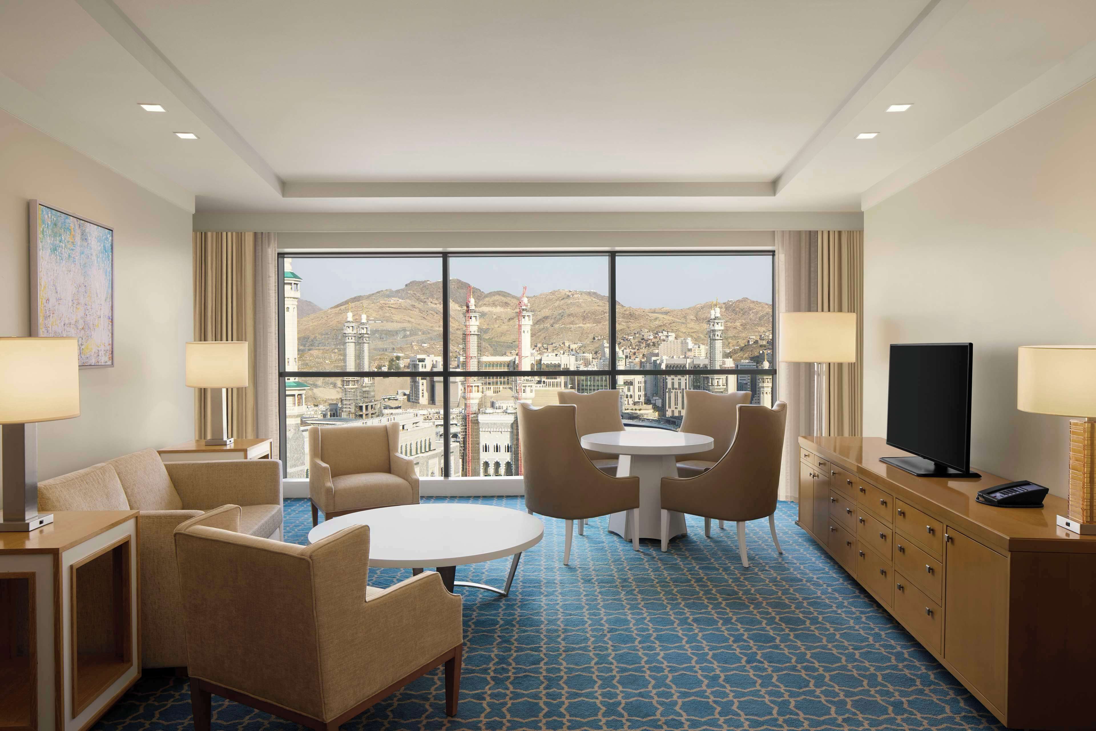 A hotel room with a large window, a round table, and a TV on a cabinet.