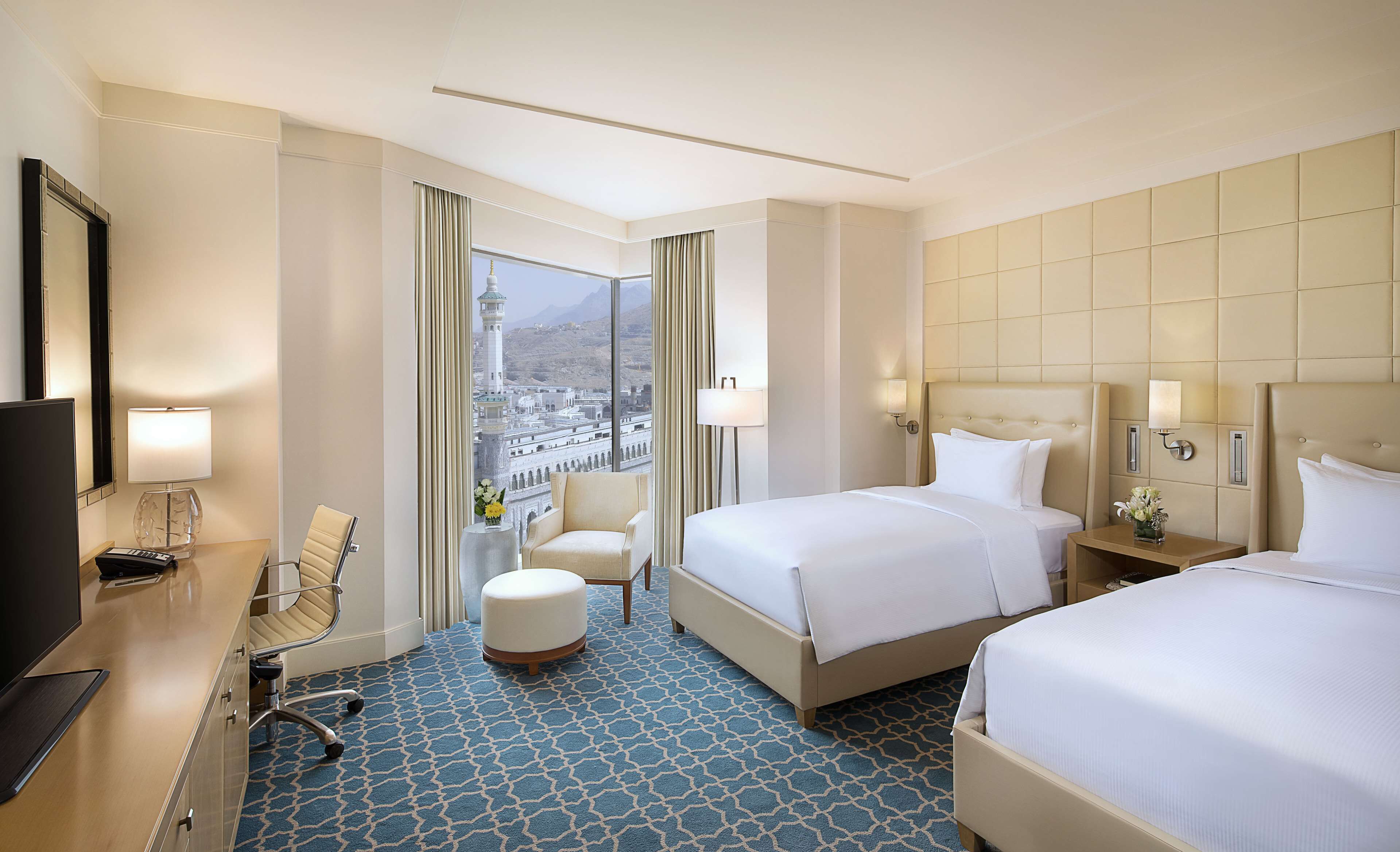 Une chambre d’hôtel avec deux lits, un bureau avec une télévision, une chaise et une vue sur le paysage urbain.