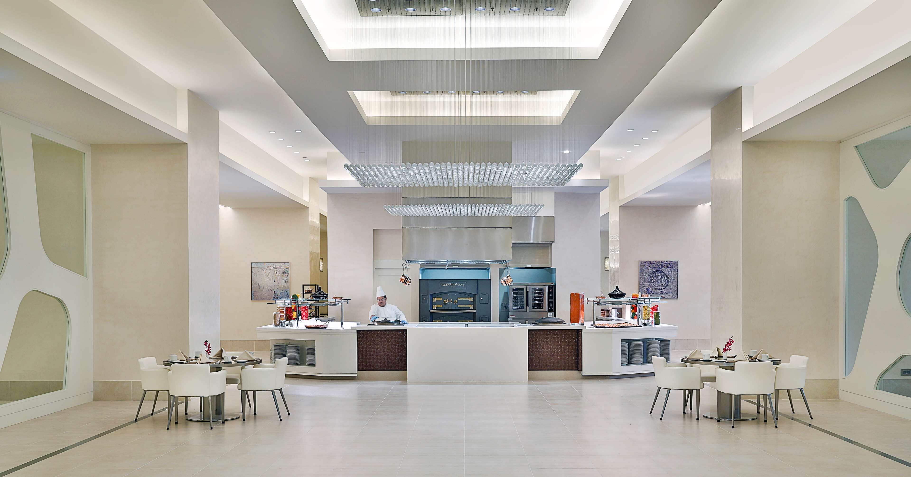 Un hall d’hôtel moderne avec un comptoir d’accueil central, des espaces de détente et une grande cuisine en arrière-plan.