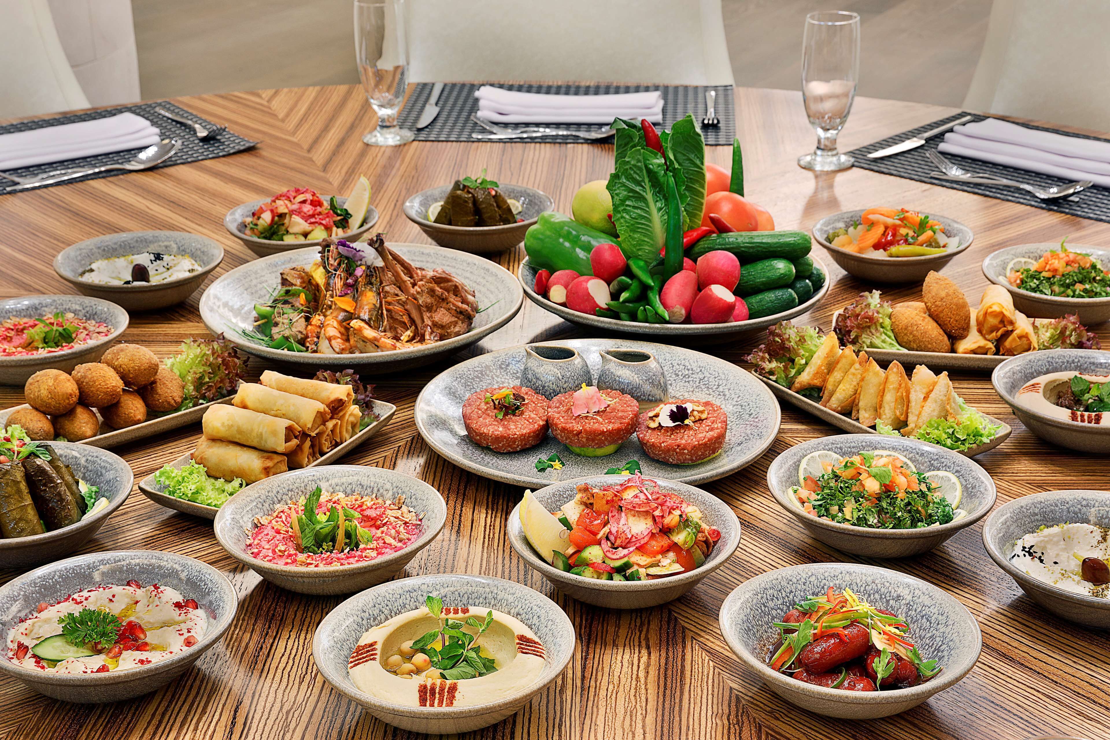 A wooden dining table with various dishes and bowls of food, arranged on a placemat.