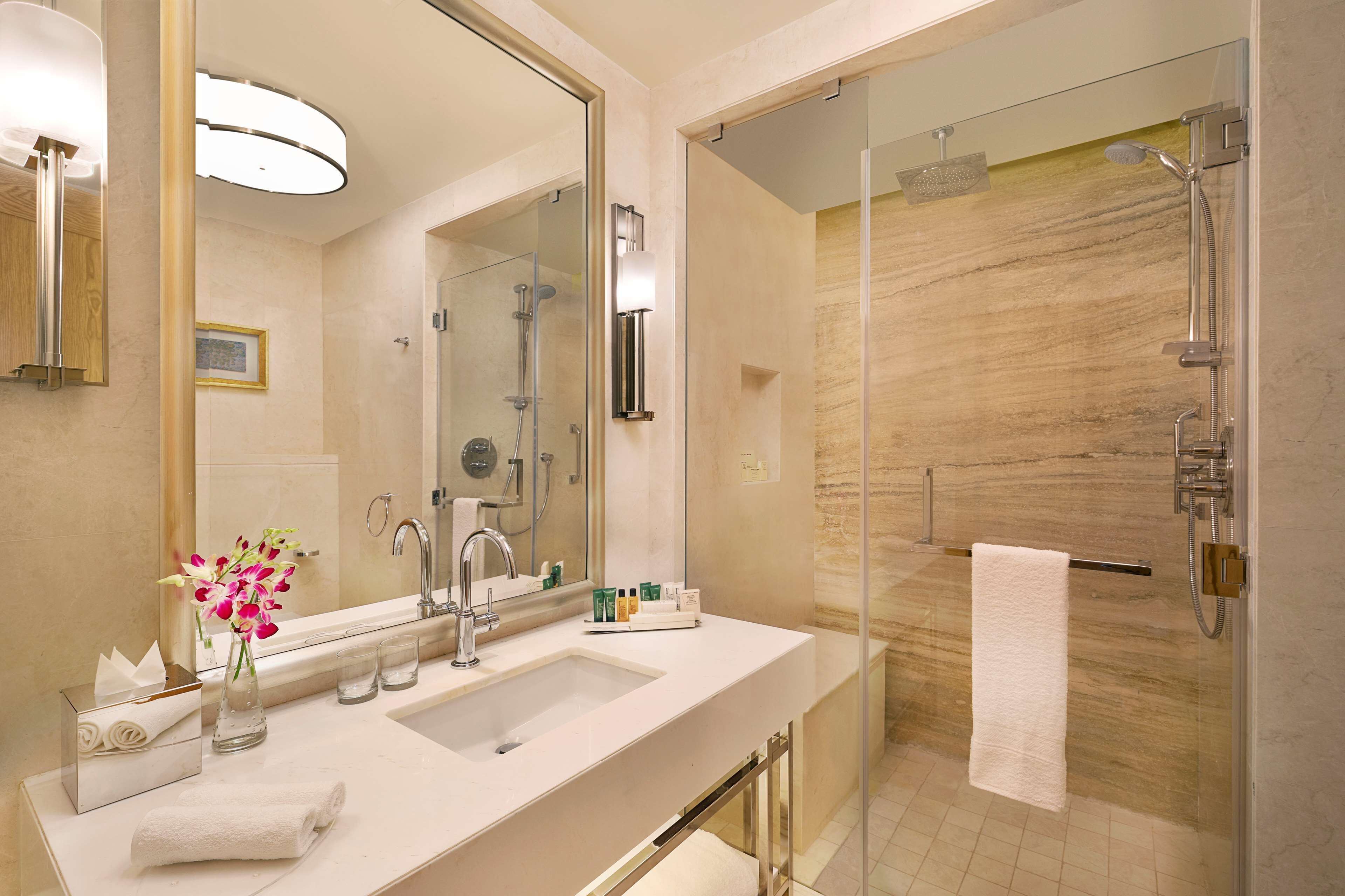 A modern bathroom with a large mirror, a sink, and a glass-enclosed shower area.