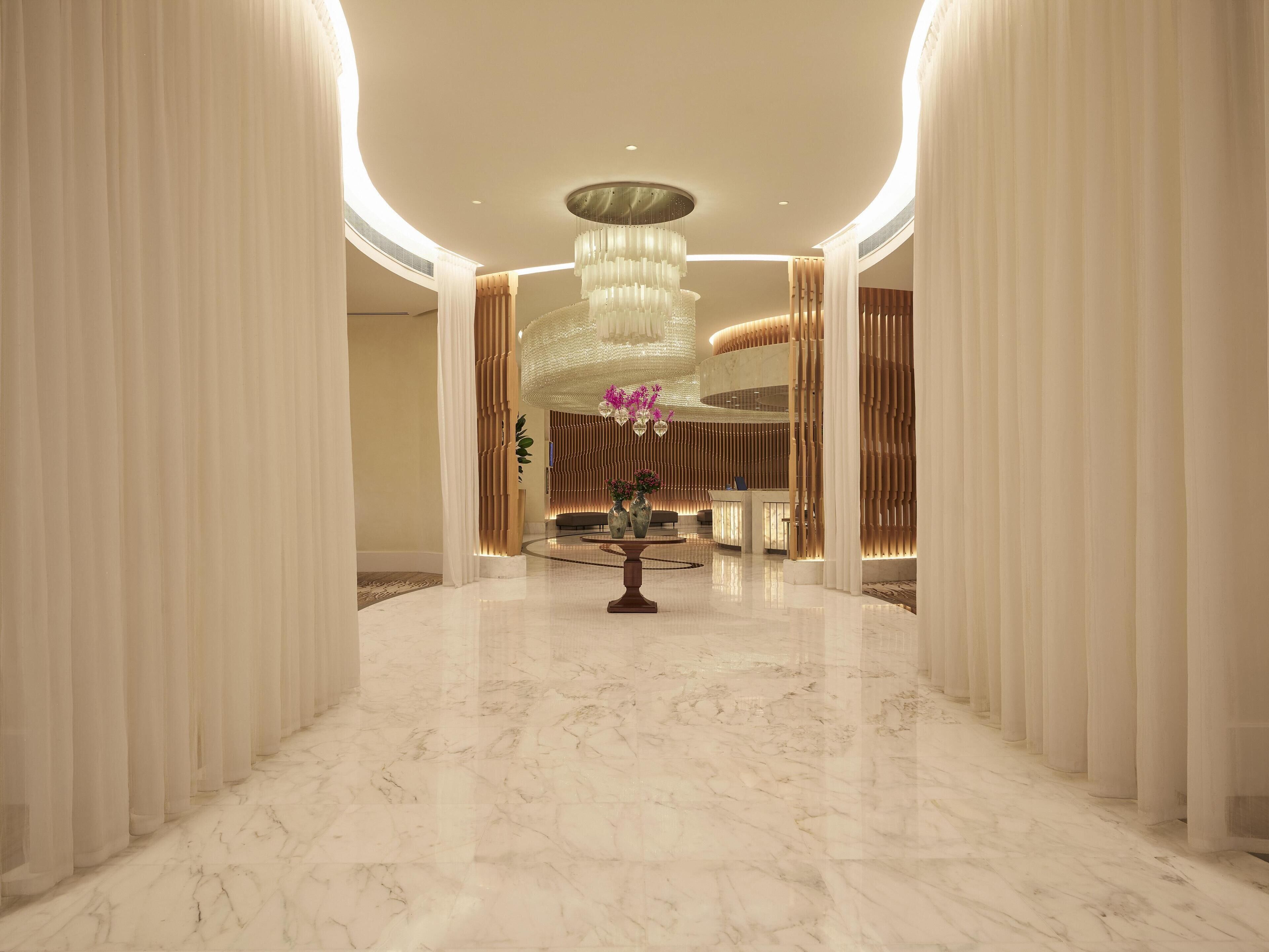 A spacious lobby with a marble floor, a reception desk, and a large chandelier.
