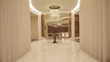 A spacious lobby with a marble floor, a reception desk, and a large chandelier.
