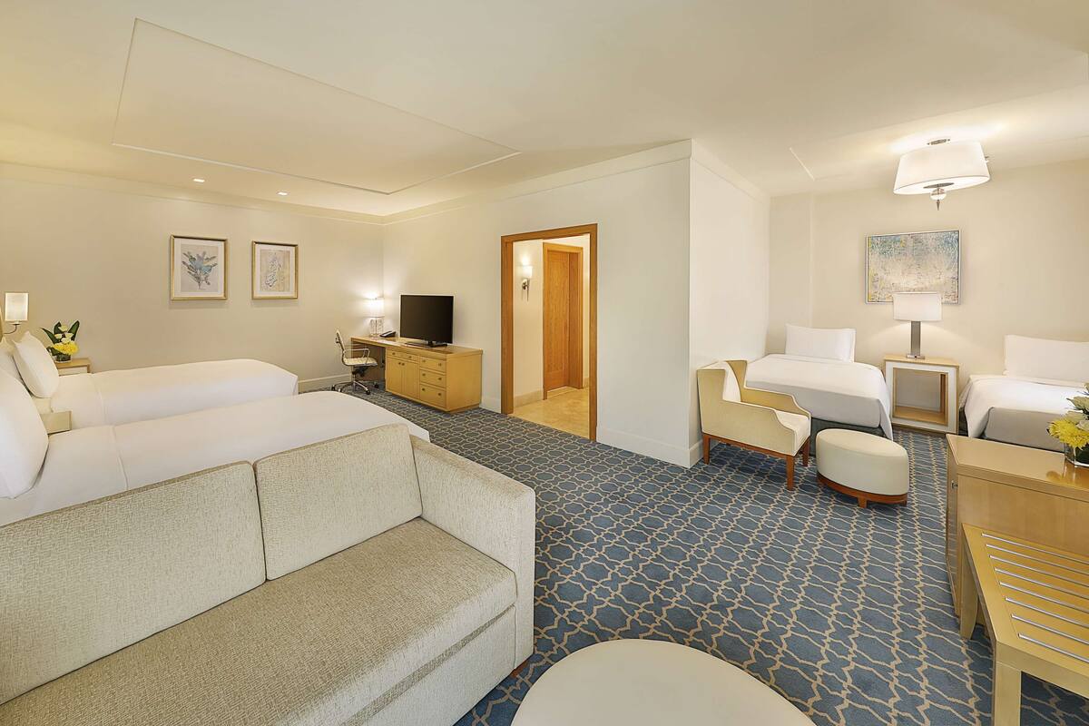 A hotel room with a large bed, a desk with a computer, a chair, a small table, and a TV.