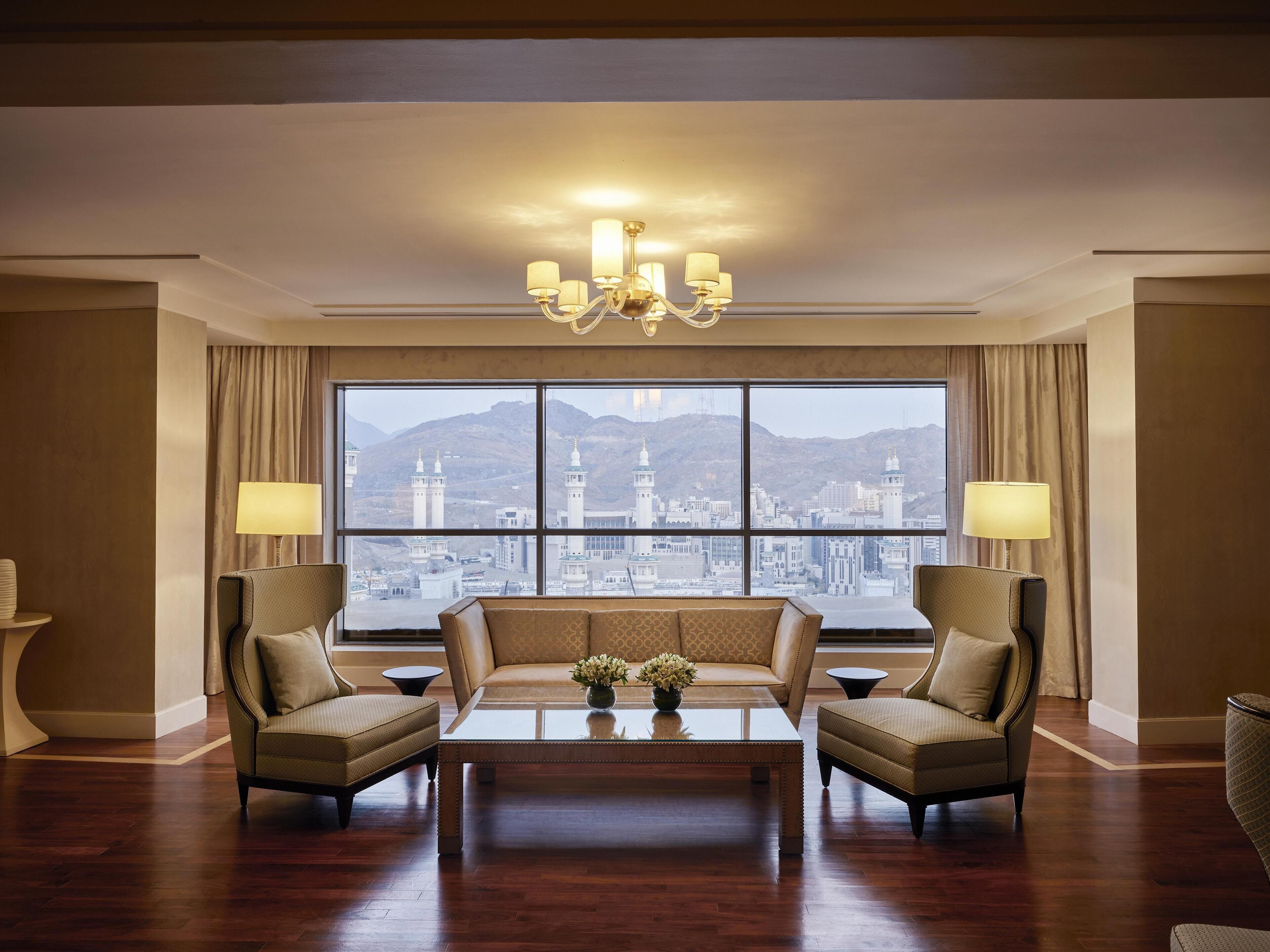 A spacious room with a large window offering a cityscape view, a chandelier, and a sofa with two armchairs.