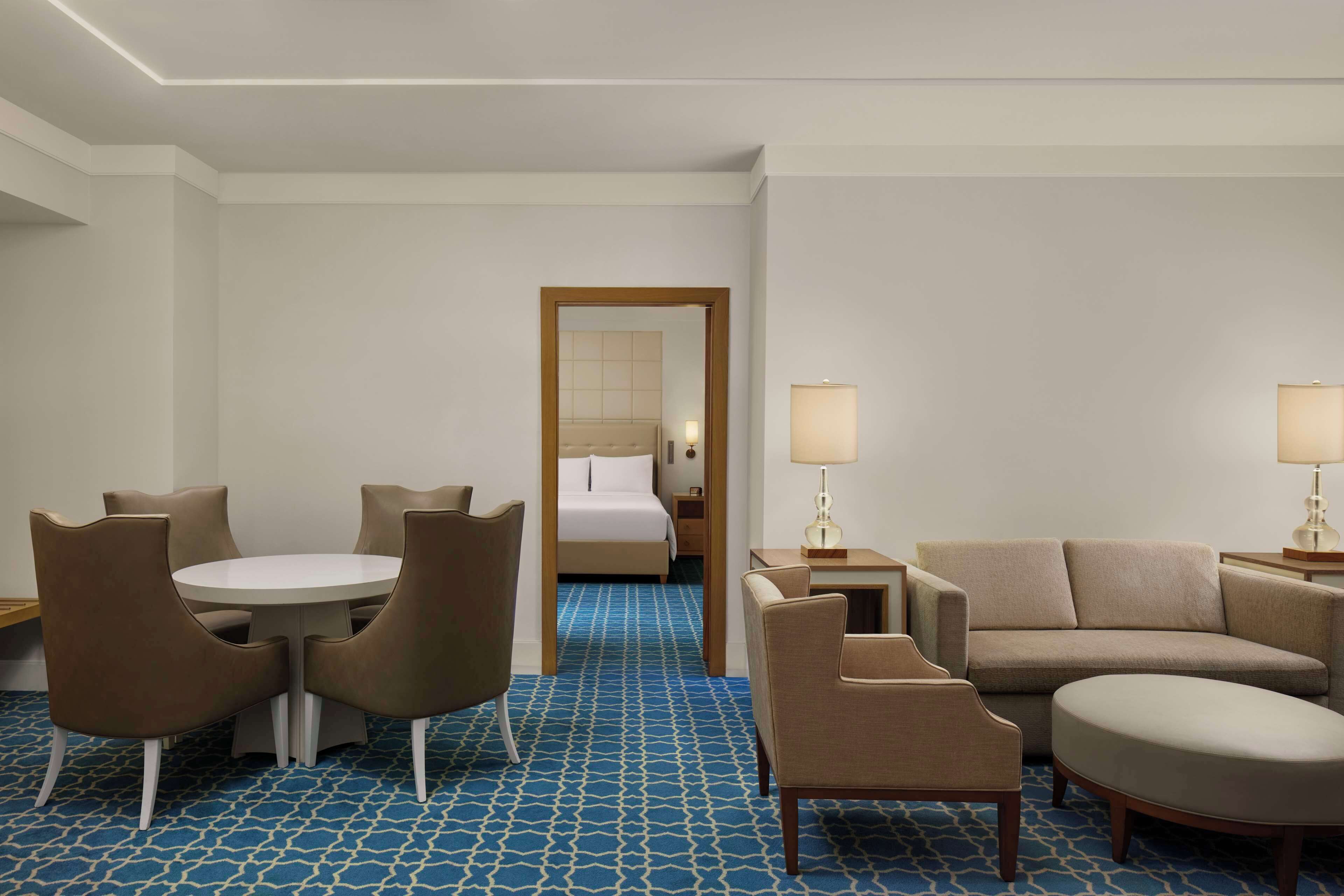 Ein Hotelzimmer mit einem Bett, einem runden Tisch mit Stühlen, einer Couch und zwei Nachttischlampen.