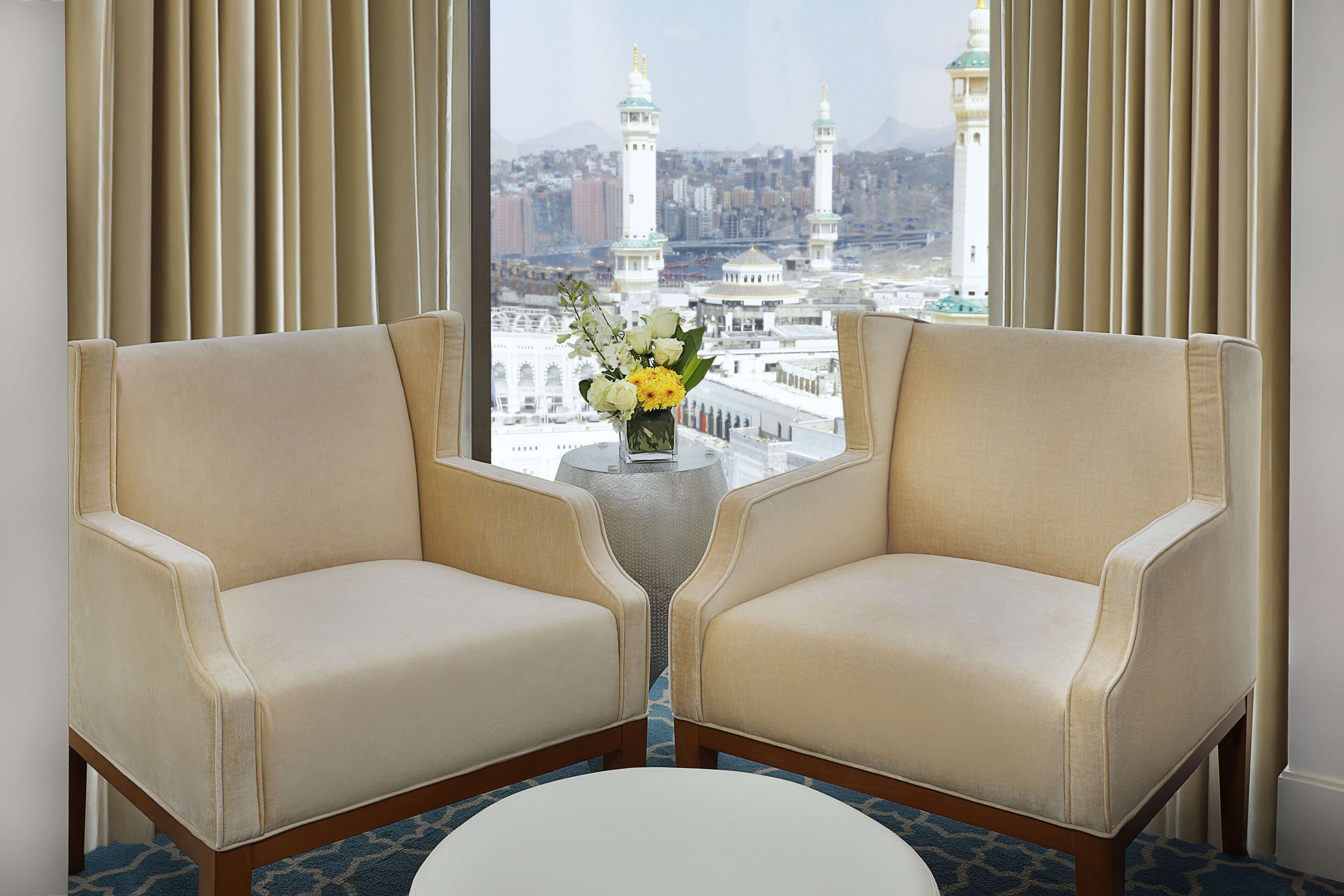 Two armchairs facing each other with a small table and vase between them, overlooking a view of a mosque with minarets.