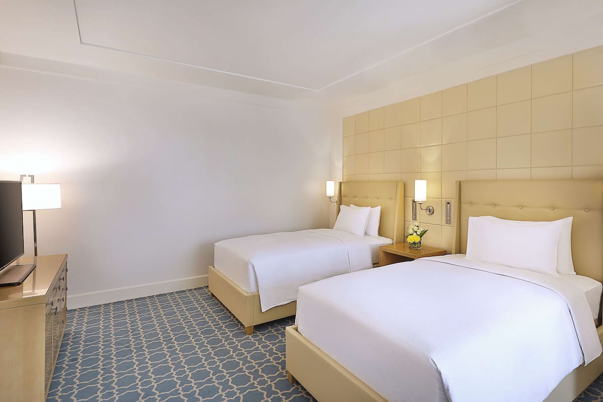 A hotel room with two beds, a TV, and a desk.