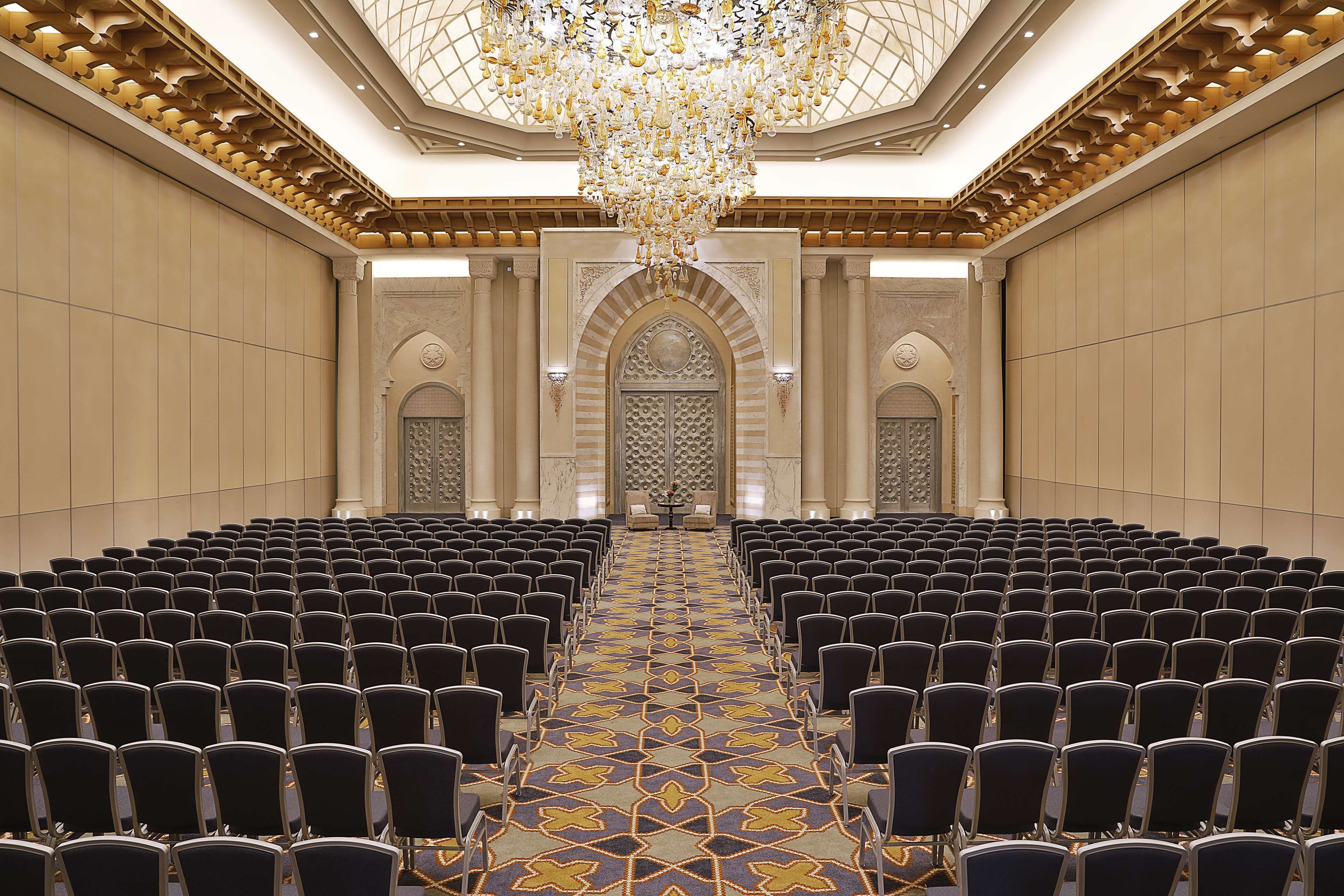A conference room with rows of chairs, a patterned carpet, and a large chandelier.
