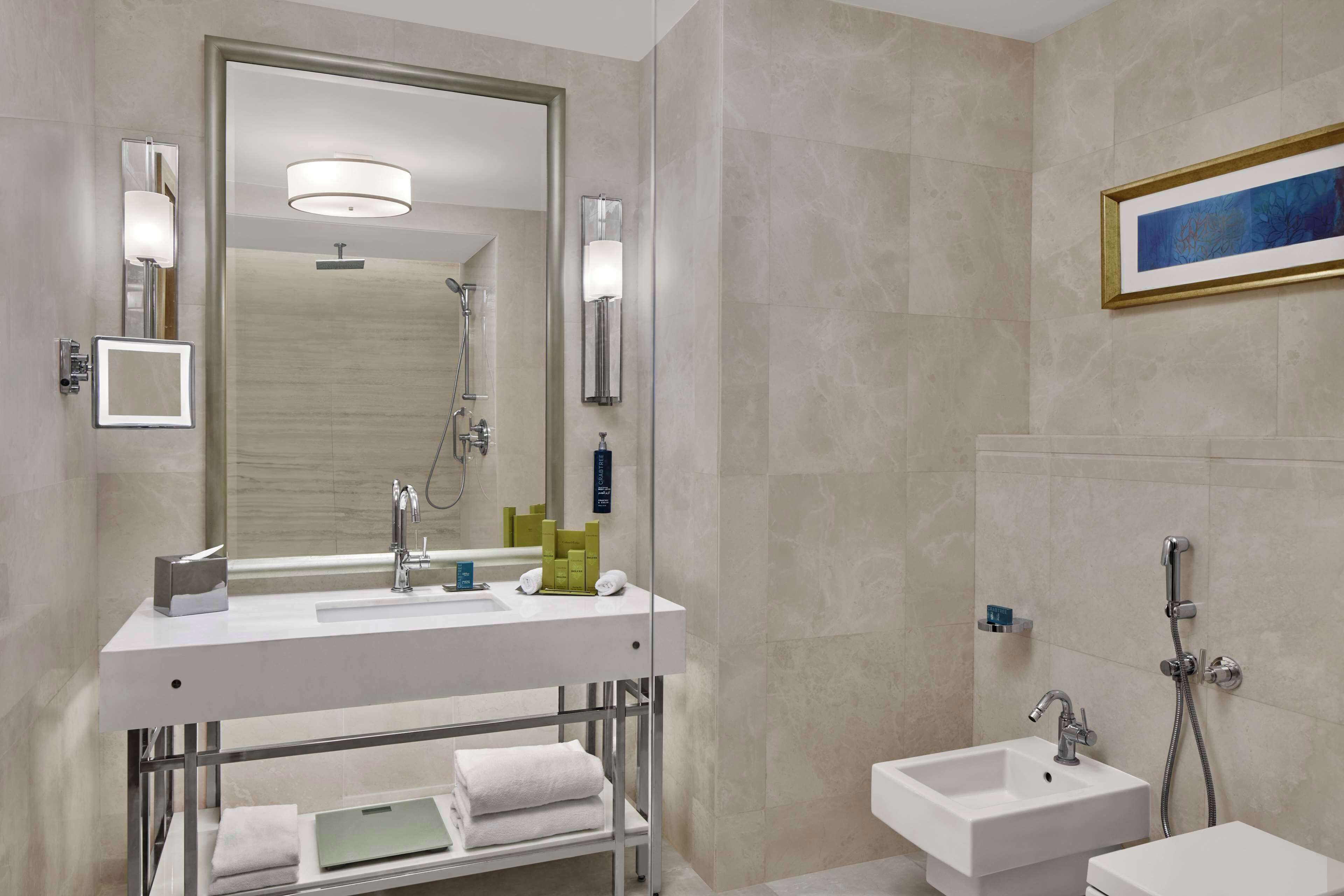 A modern bathroom with a large mirror, a vanity with a sink, a shower area, and a framed artwork on the wall.