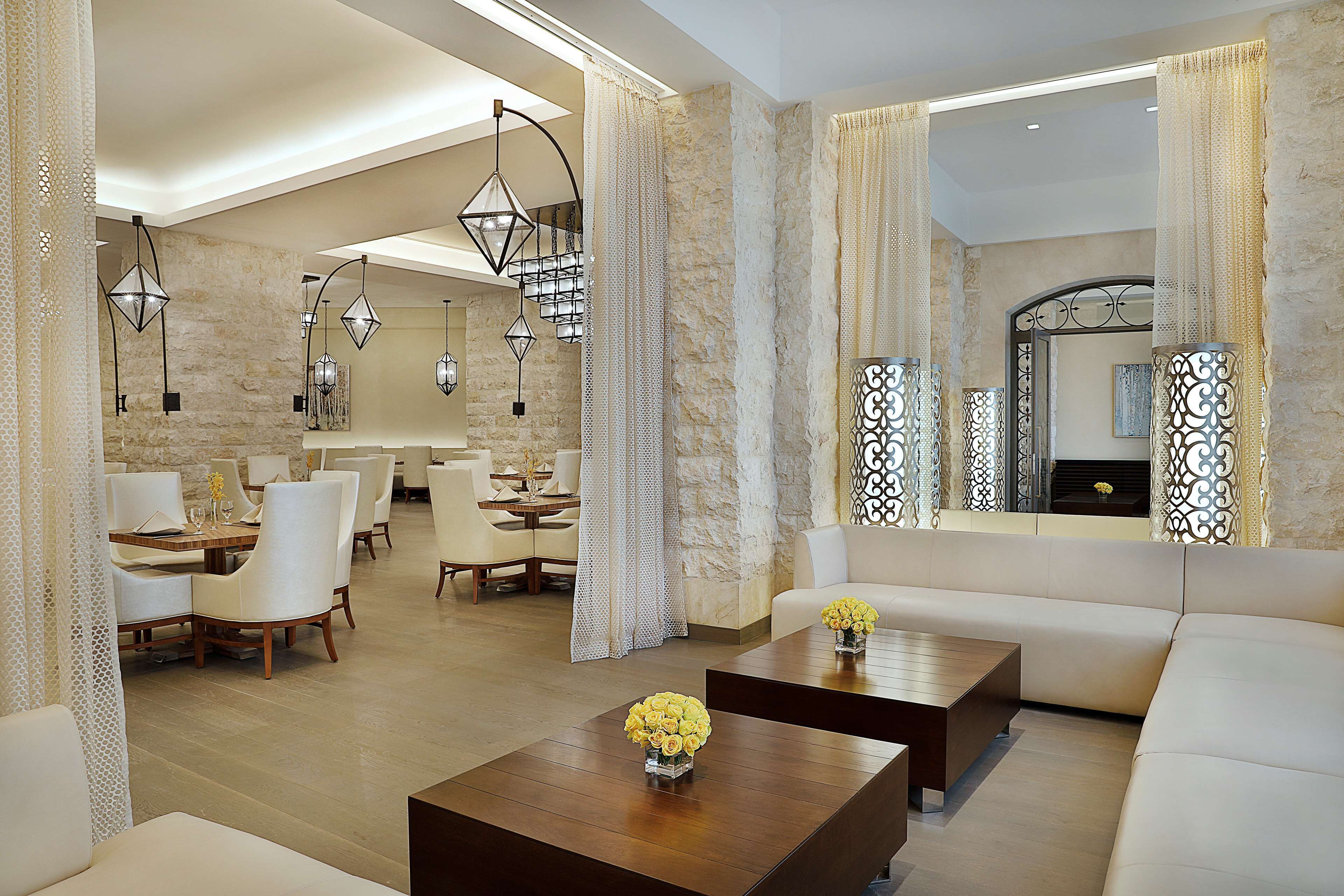 A spacious lobby with a modern design, featuring a seating area with sofas and chairs, a coffee table with flowers, and a staircase with a unique light fixture.