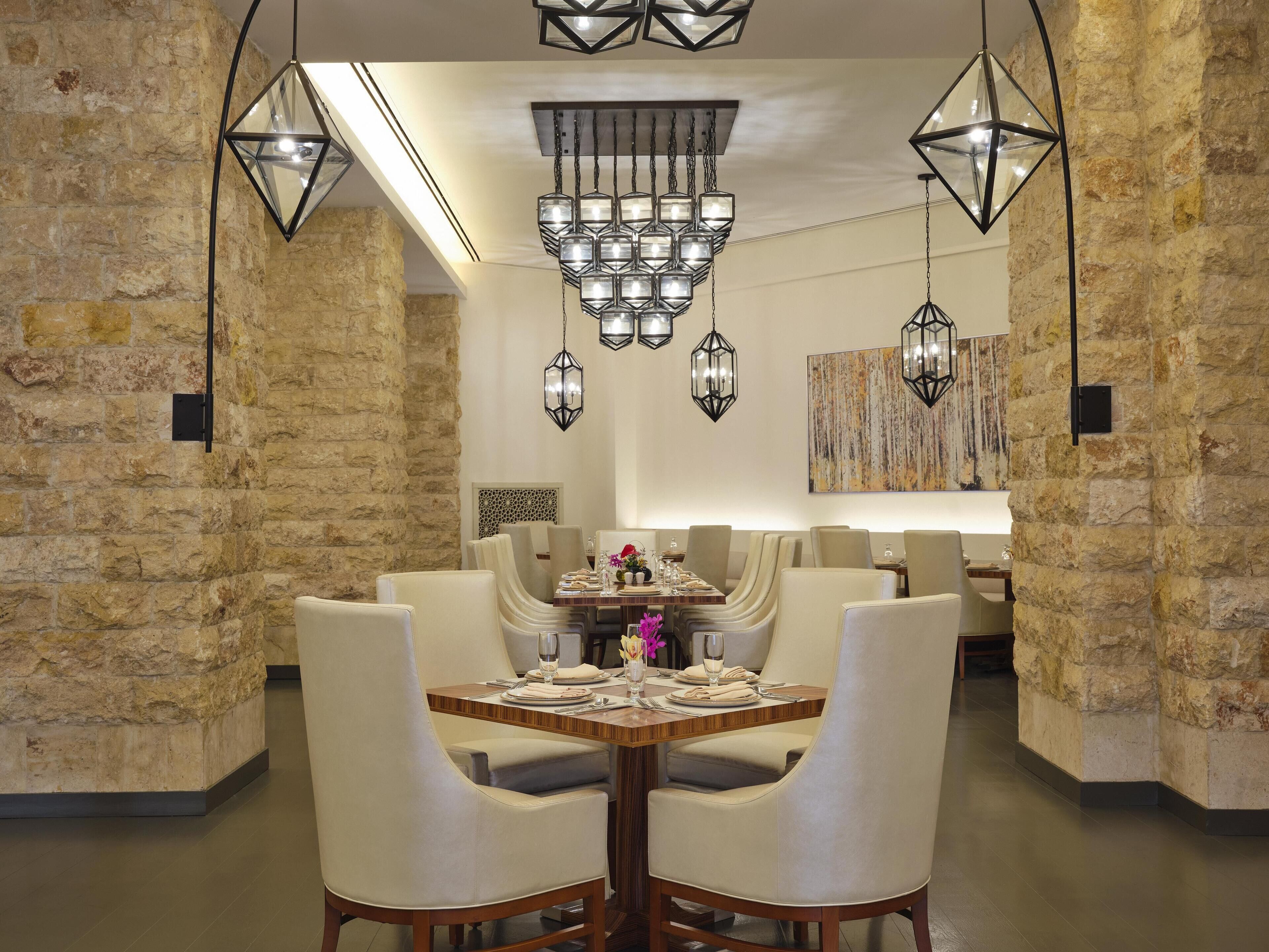 A dining area with a stone wall, a wooden table set for four, and hanging hexagonal lanterns.