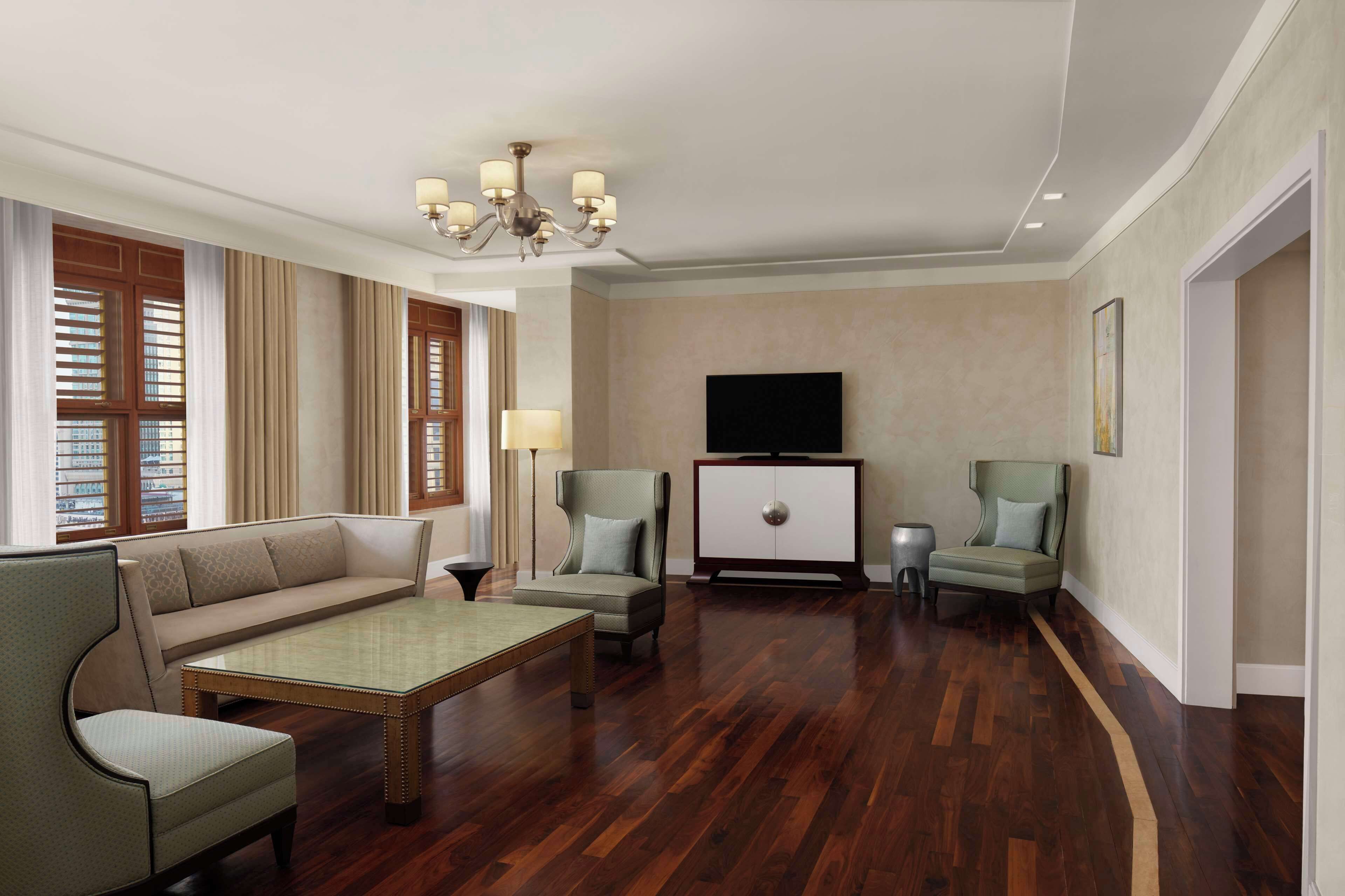 Un salon spacieux comprenant un canapé, deux fauteuils, une table basse, un téléviseur et un lustre.
