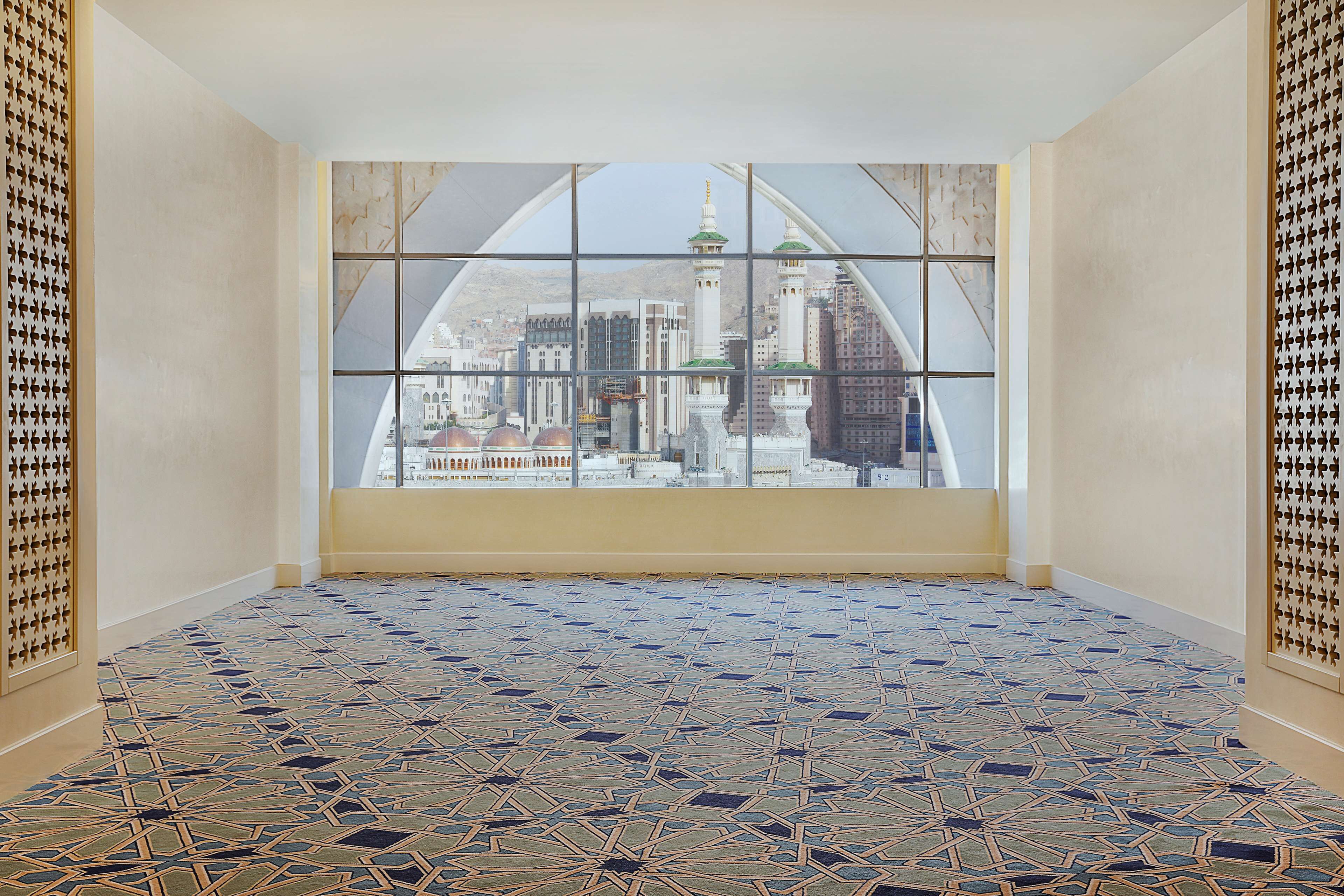A room with a large window offering a view of a cityscape, including a mosque with two minarets. The floor has a geometric patterned tile design.