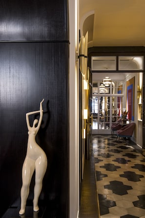 Un pasillo con suelo a cuadrícula blanco y negro, una escultura blanca y un comedor con sillas y una mesa.