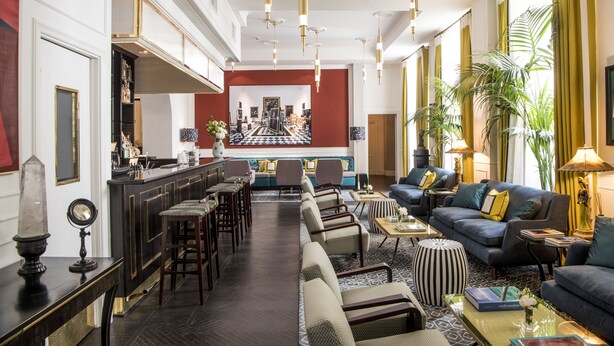 A spacious lobby with a long bar, seating area, and a view of the kitchen in the background. - Hotel Vilòn (Rome)