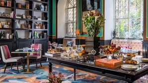 A room with a dining table set with various food items, a bookshelf filled with books and decorative objects, and a large window with a view of greenery. - Hotel Vilòn (Rome)